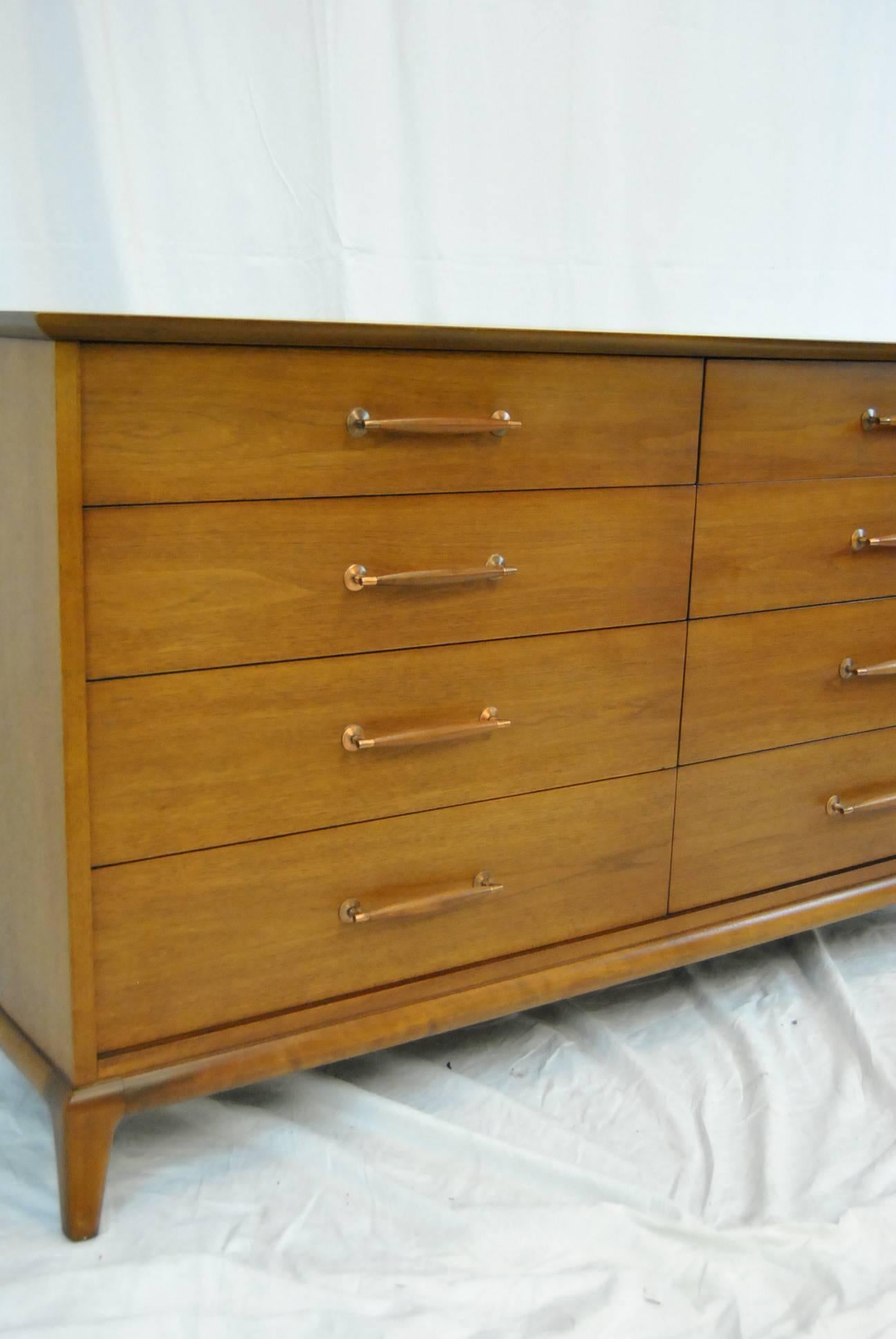 A beautiful walnut eight drawer dresser by Henredon as part of their circa 1960 collection. Dresser has eight dovetailed drawers with atomic age handles of tapered wood and brass. Four top drawers are divided and the two top have gentlemen’s change