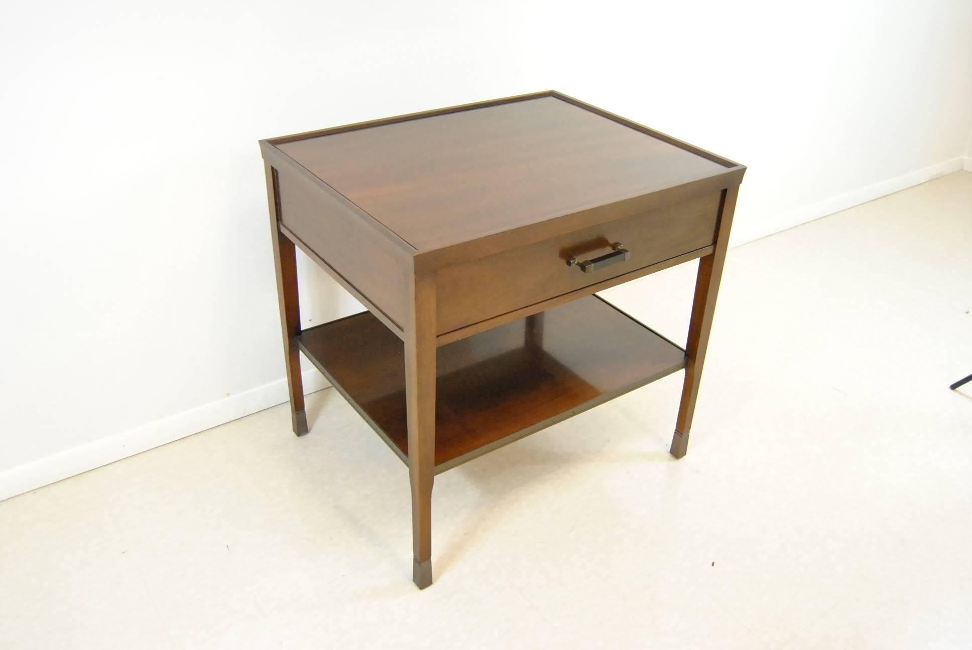 A walnut side table by Bill Sofield for Baker Furniture. This attractive table features antique bronze trim around the bottom shelf and the legs caps. The hardware is wood with bronze and it has dovetailed drawers.