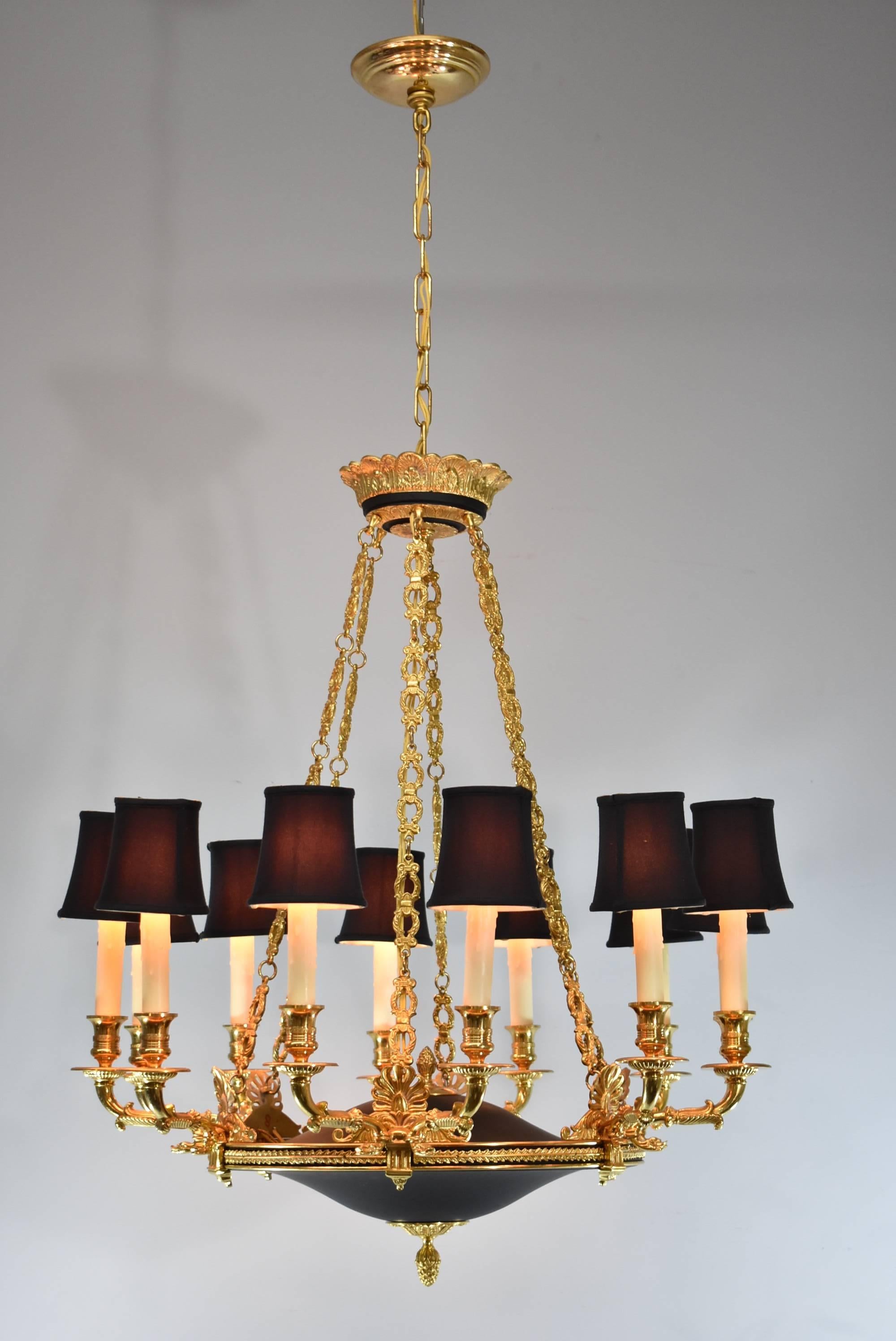 An elegant Italian 12 light bronze and black ebonized chandelier. This stunning light fixture features six chains that drape down from the center crown. In front of each chain there are double arms mounted with dolphin heads. It has a spun brass