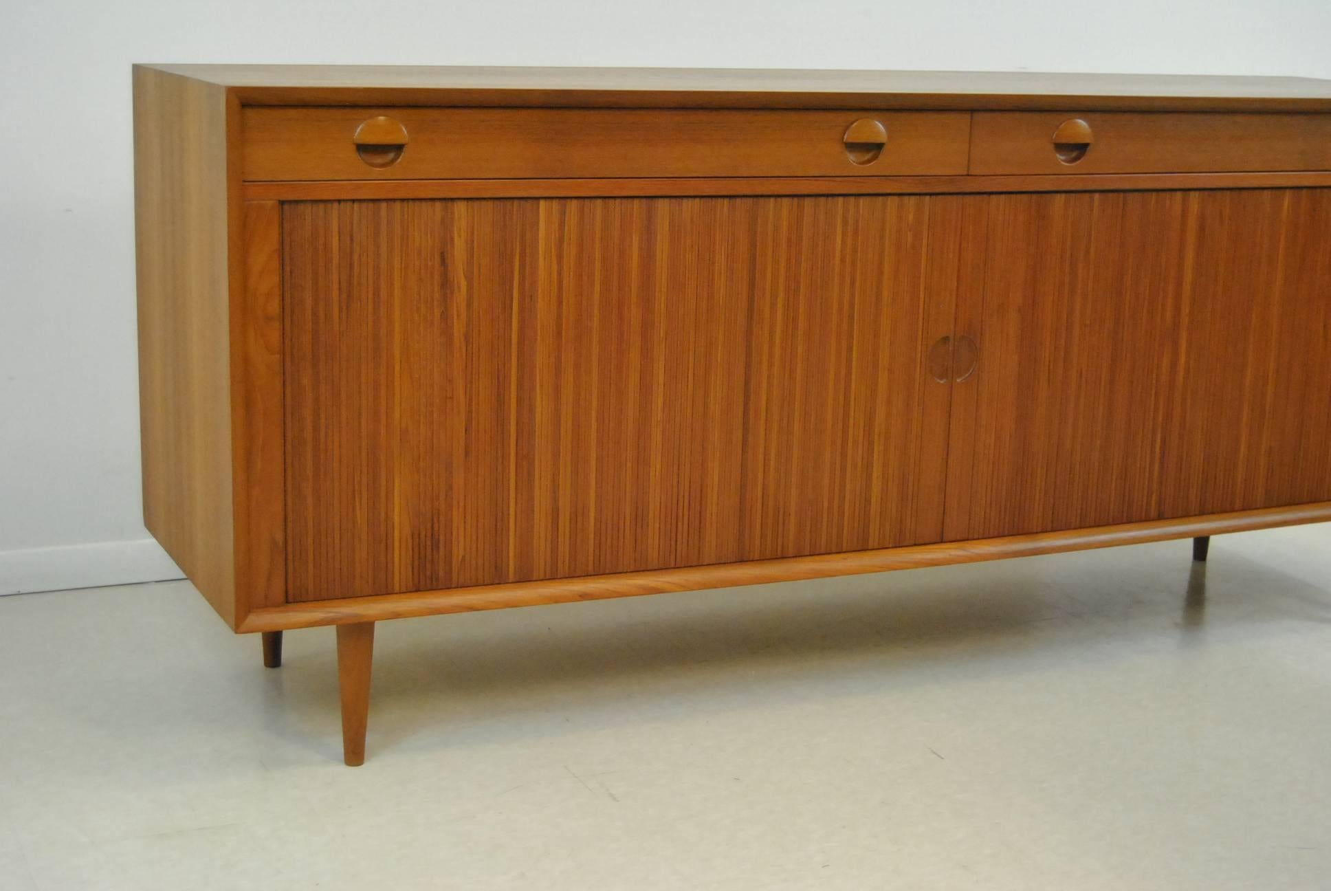 A great 71.5" long Danish Modern teak credenza designed by Grete Jalk for Sibast. The credenza features two tambour doors and two drawers. The two tambour doors open to storage areas with one adjustable shelf. The drawers feature "cat's