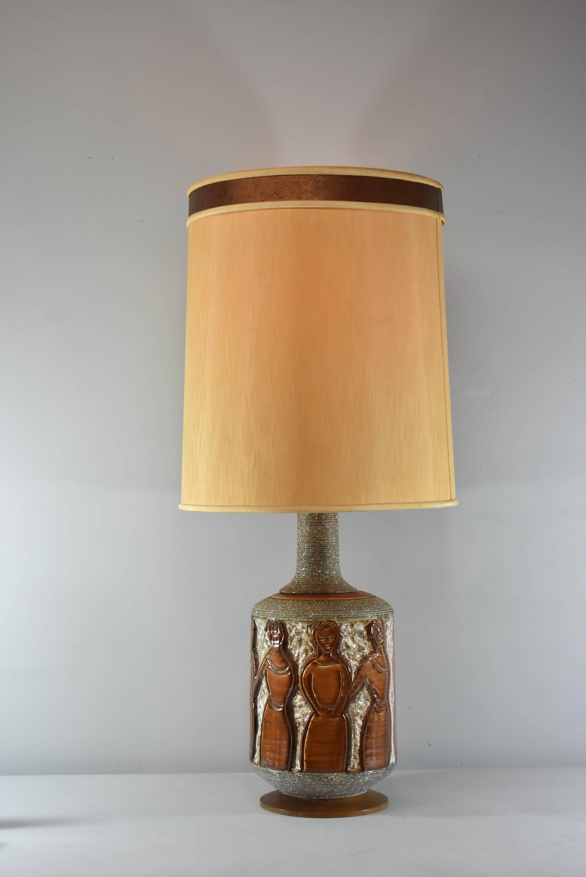 A Mid Century figural table lamp by Fratello Faniullacci. This stunning lamp features brown, raised stylized figural females that encircle the base. There is also a textured wound string detail on the neck of the base and the bottom is wood. Single