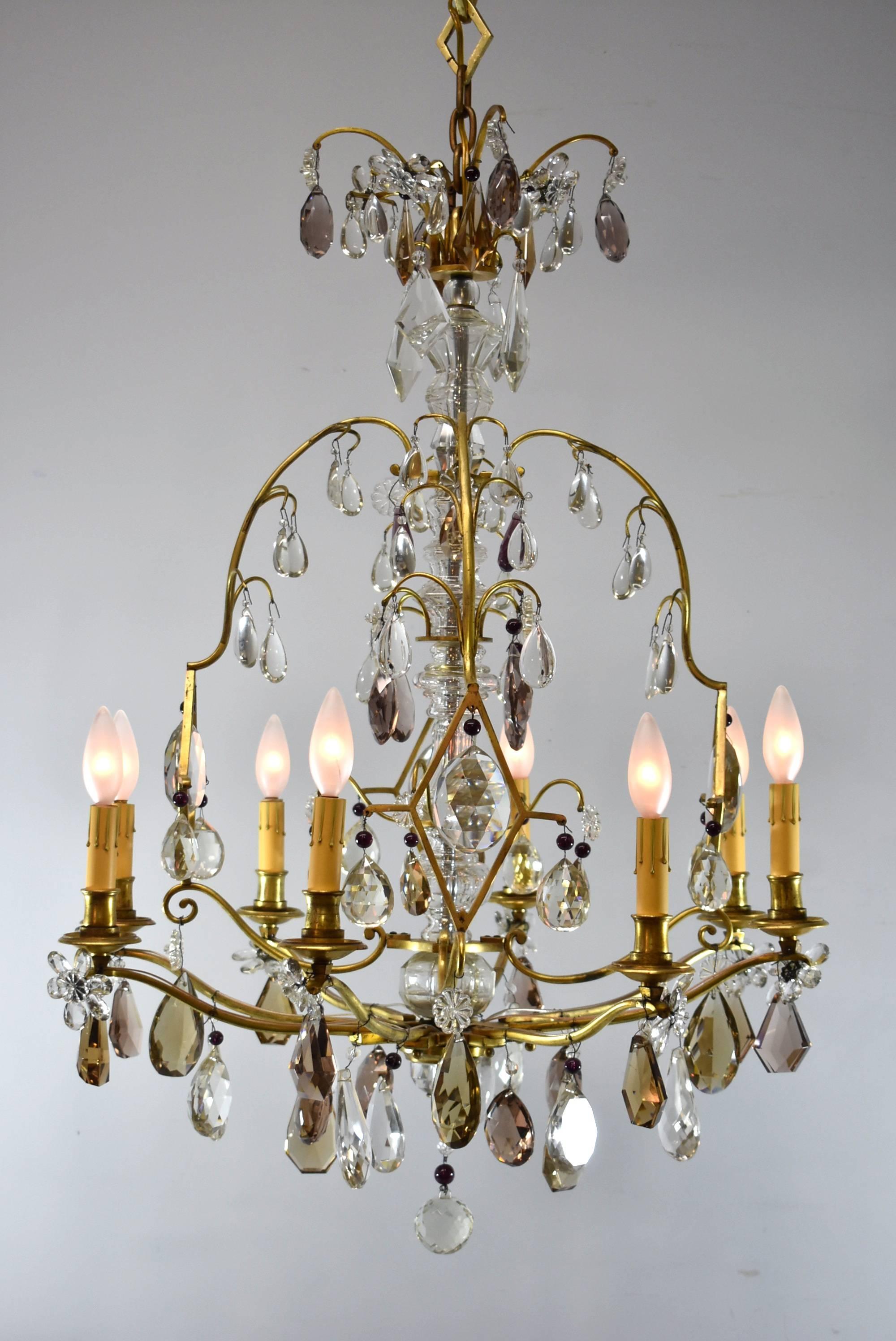 Uno splendido lampadario francese in ottone e cristallo. Cornice a volute in metallo dorato con forme di diamante che racchiudono prismi, albero di cristallo e accenti floreali, appeso con prismi di cristallo di topazio, ametista e incolore. Timbro