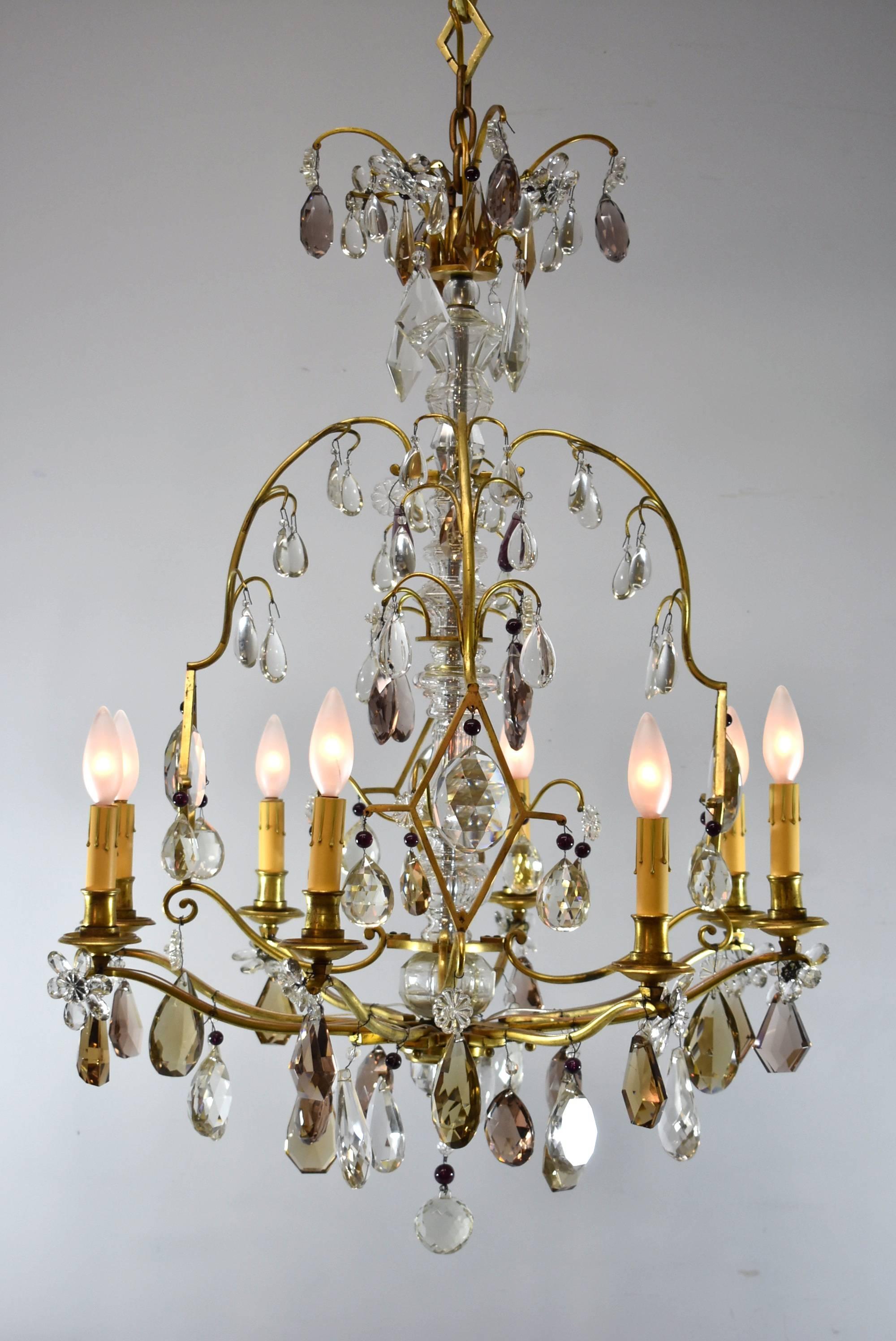 A stunning French brass and crystal chandelier. Gilt metal scroll frame with diamond forms enclosing prisms, crystal shaft and floral accents, hung with crystal prisms in topaz, amethyst and colorless. Stamped made in France. Very good condition