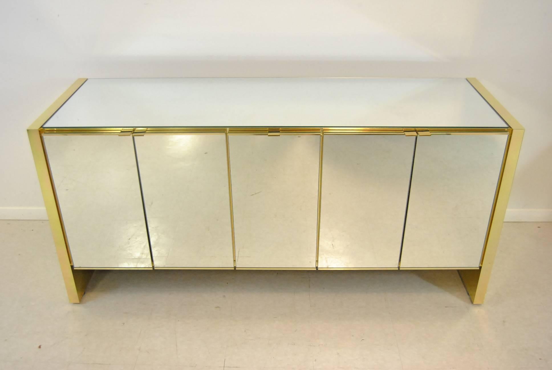 A fabulous Mid-Century Modern credenza by Ello. It features a mirrored top and mirrored doors with brass supports and adjustable shelves. Very good condition with one small ding on the top right rear brass edge and a few light scratches on top.
