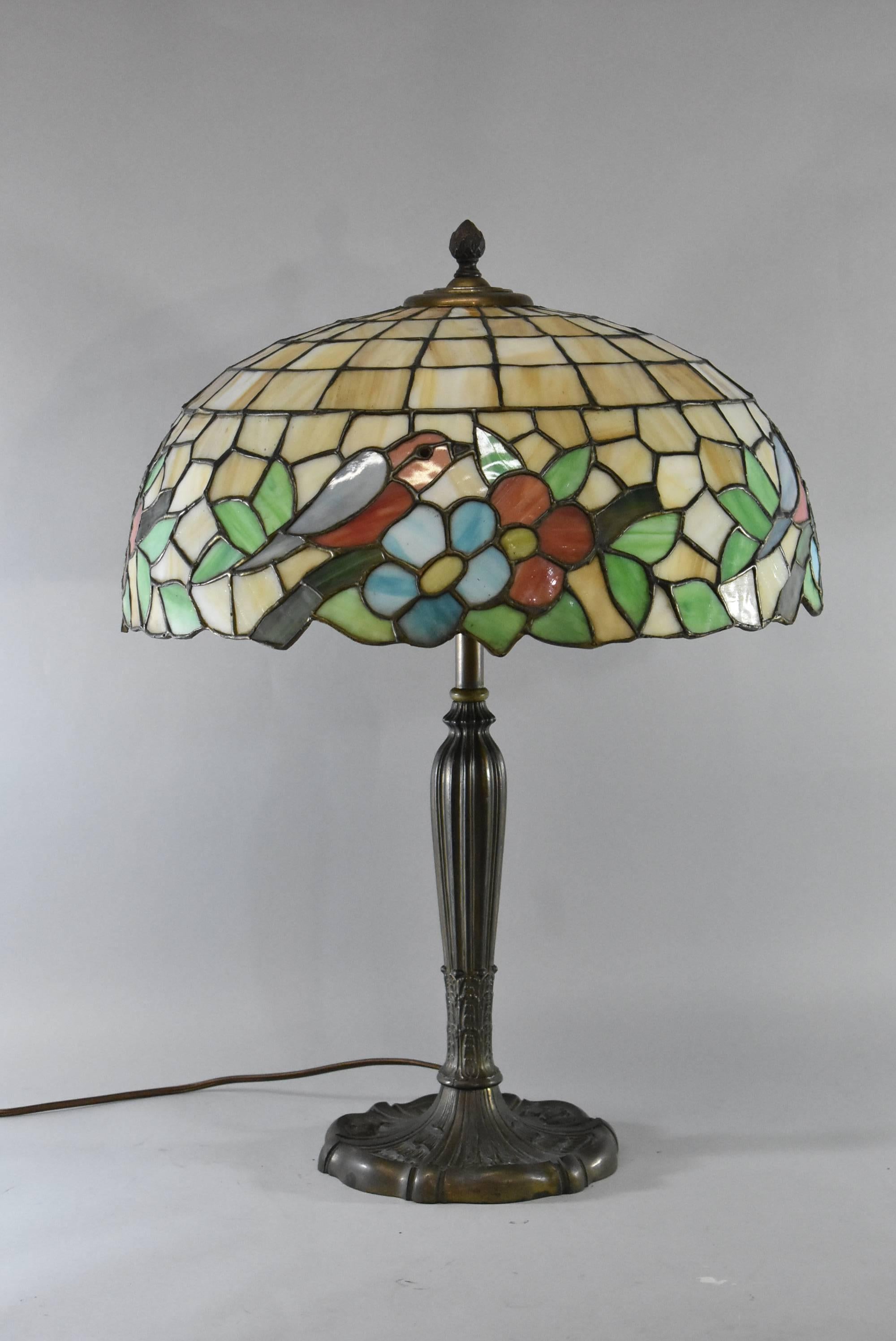A stunning bent panel leaded glass lamp by Miller Lamp Company. Signed on the bottom MLCO and 232. It features a beautiful bird and flower design and original two sockets. The dimensions of the base are 25
