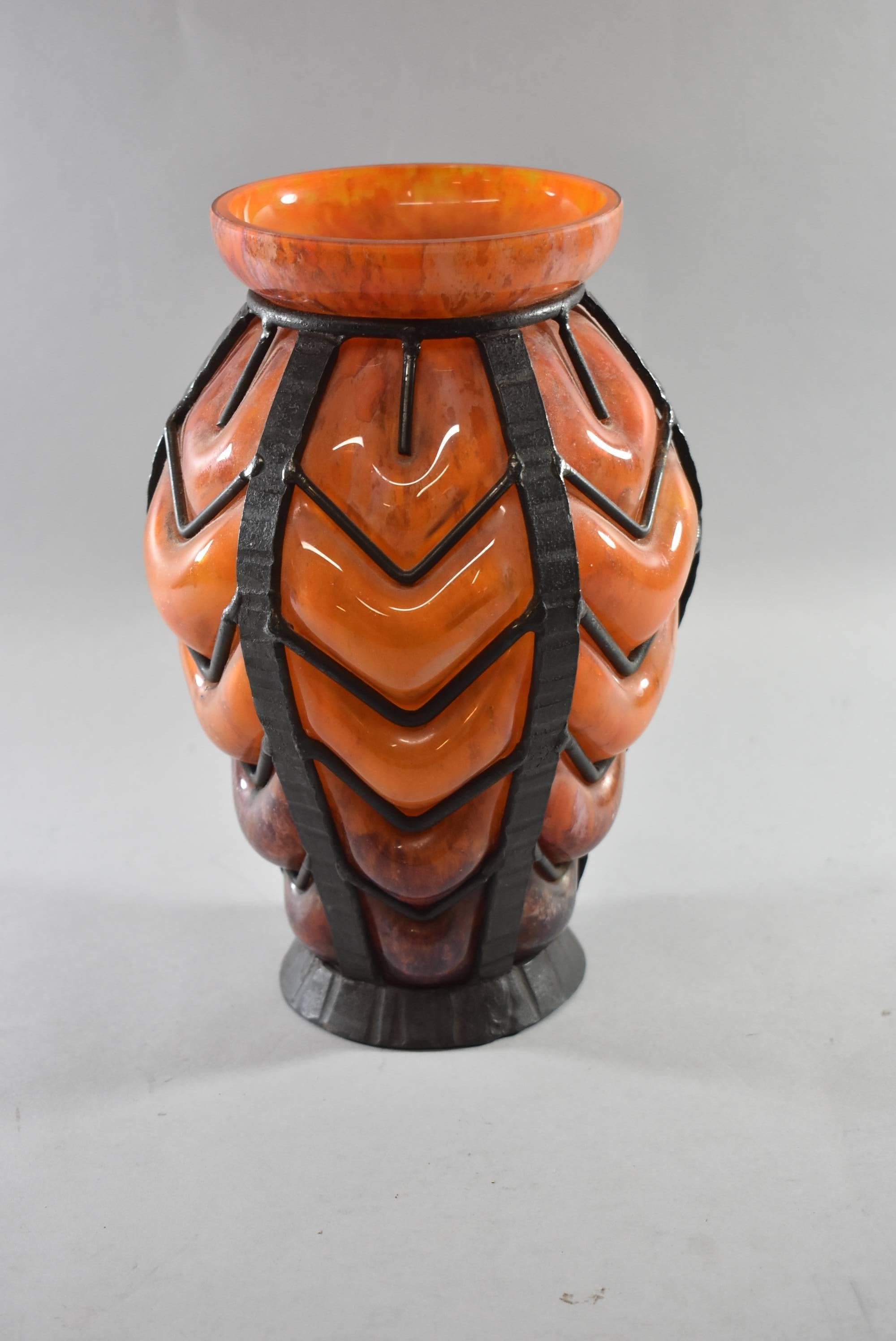 A beautiful Art Deco French art glass vase. This stunning vase features a blown glass vase encased with a hand fashioned iron frame in variegated shades of orange. Likely from the Daum factory. Great condition, no damage. Dimensions: 6.5