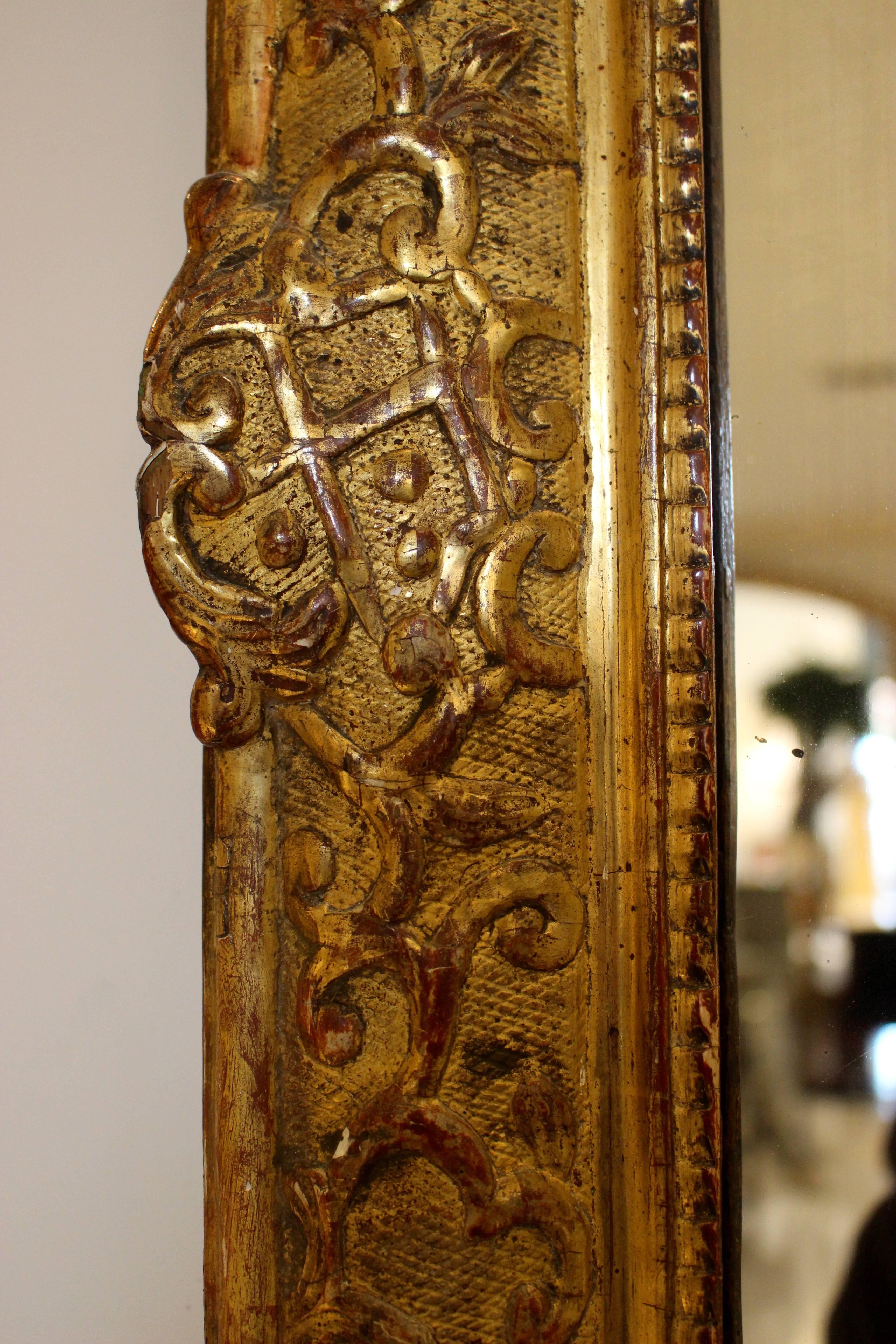 An early 18th century French giltwood mirror from the Régence period in the Baroque style. The arched rectangular mirror plate is set within a conforming molded frame carved with foliate scrolls on a lattice designed ground. Crowned by a military