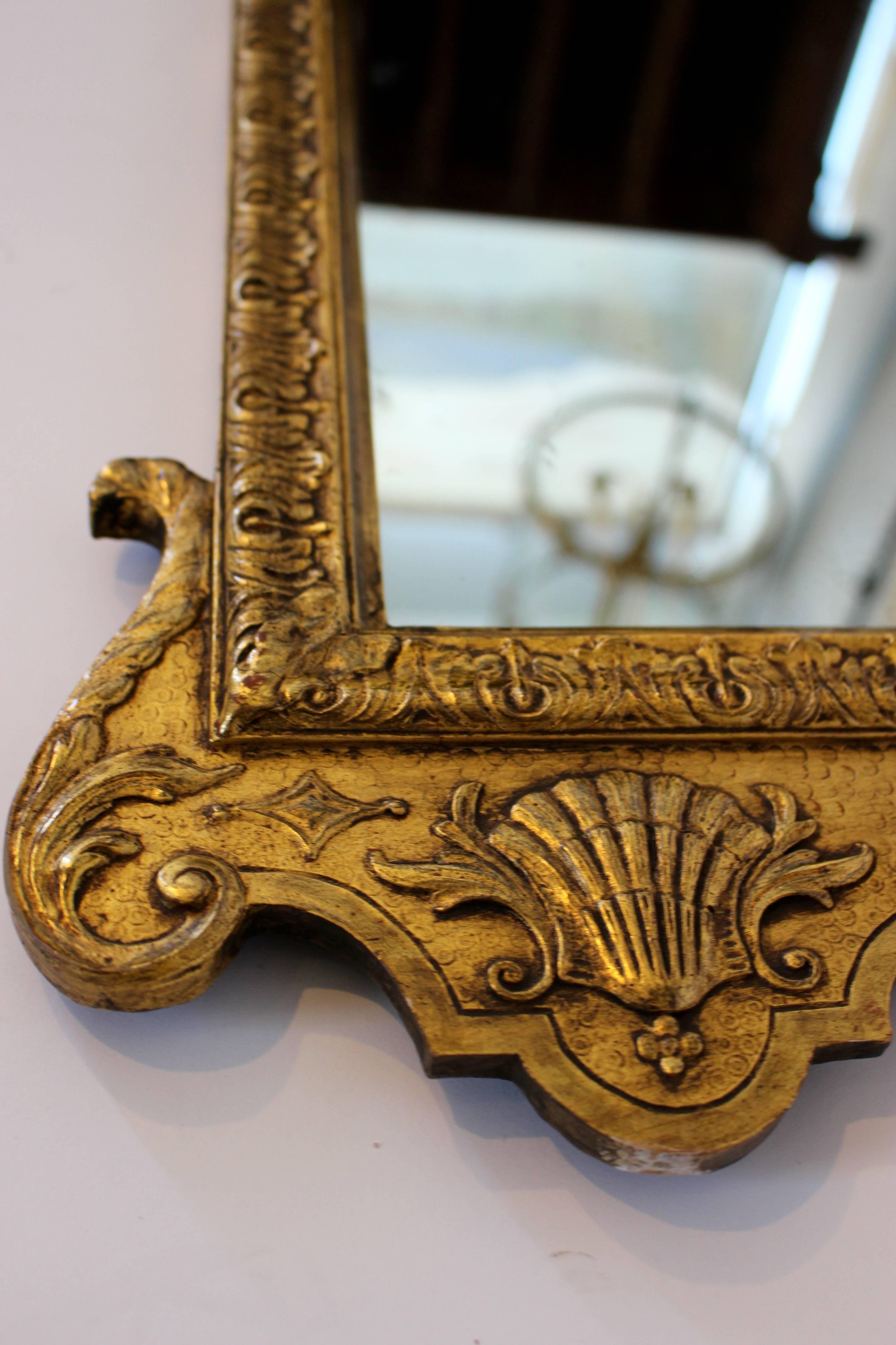 Vergoldeter Spiegel aus dem frühen 18. Jahrhundert mit geschnitztem Dekor und gebrochenem Giebel. Die originale, abgeschrägte, rechteckige Spiegelplatte mit abgerundeten oberen Ecken befindet sich in einem vergoldeten Rahmen mit geschnitztem