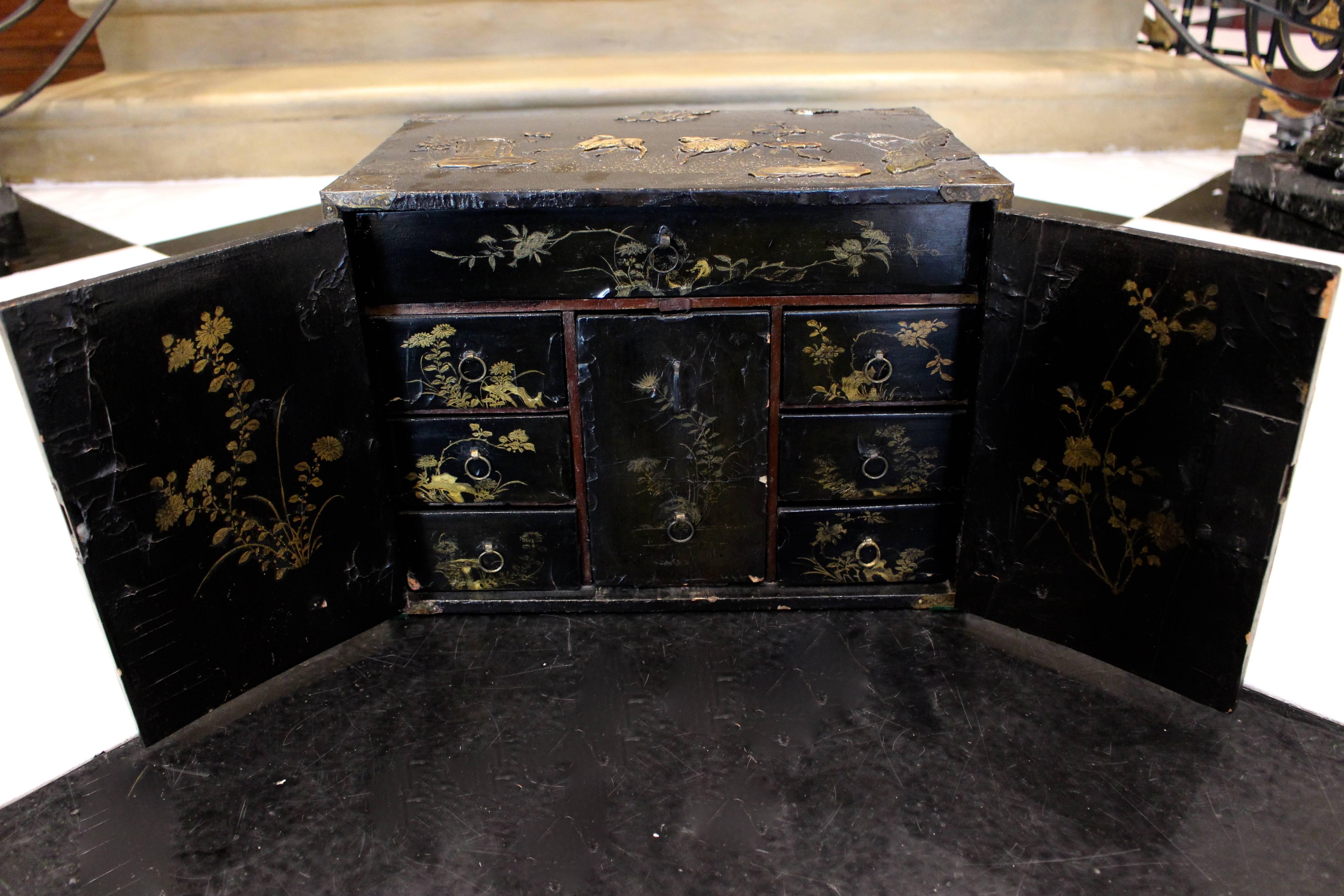 A late 18th century small Chinese black lacquered wood cabinet decorated with a raised animal scenery in a traditional landscape design. This cabinet of rectangular shape is elaborately inlaid with an array of colored stones in raised designs of