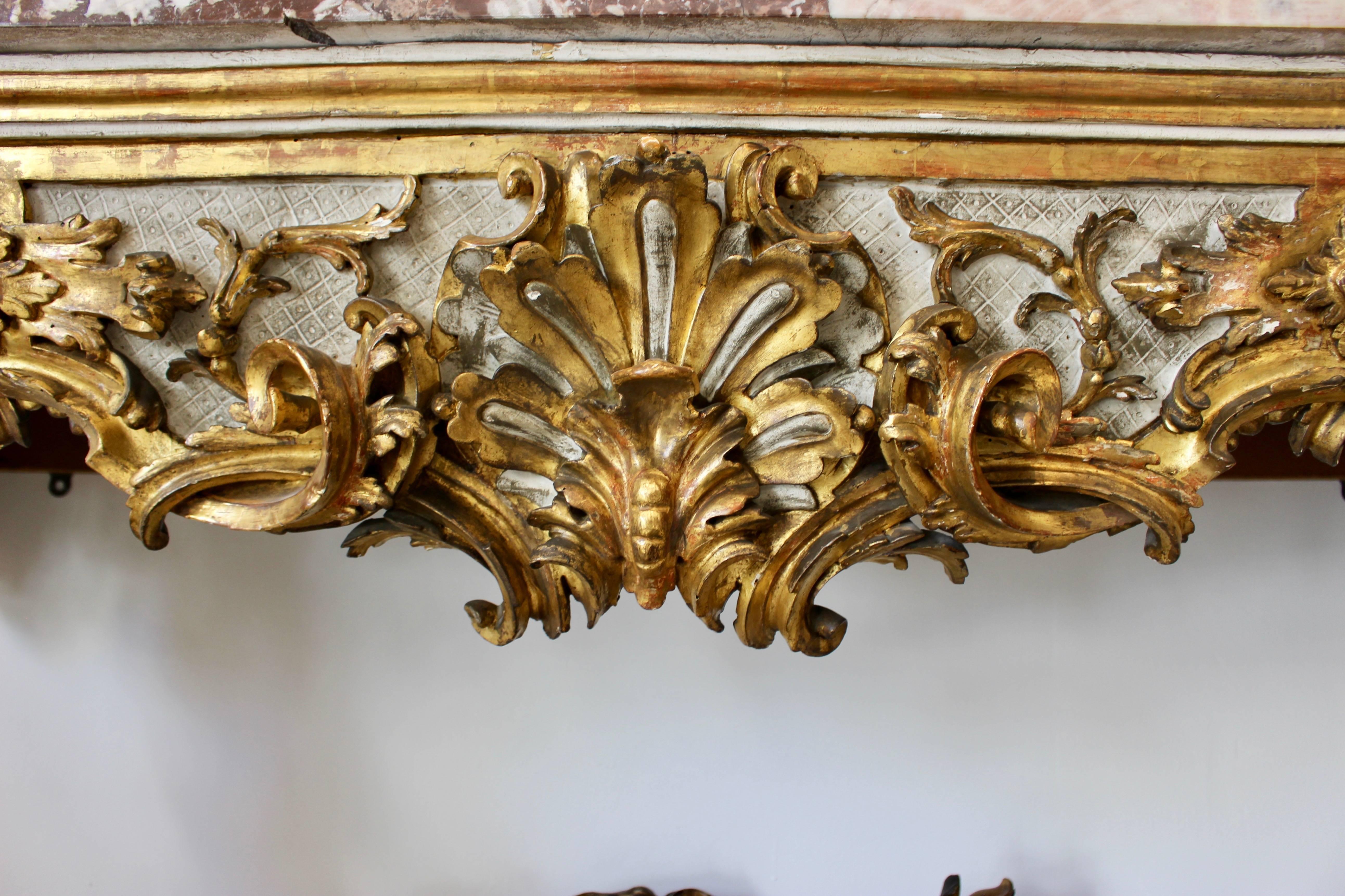 An Venetian early 18th century Rococo period carved giltwood console table with red variegated marble top and painted accents. This Italian console table features a rectangular variegated marble top, sitting above a stunning carved giltwood base,