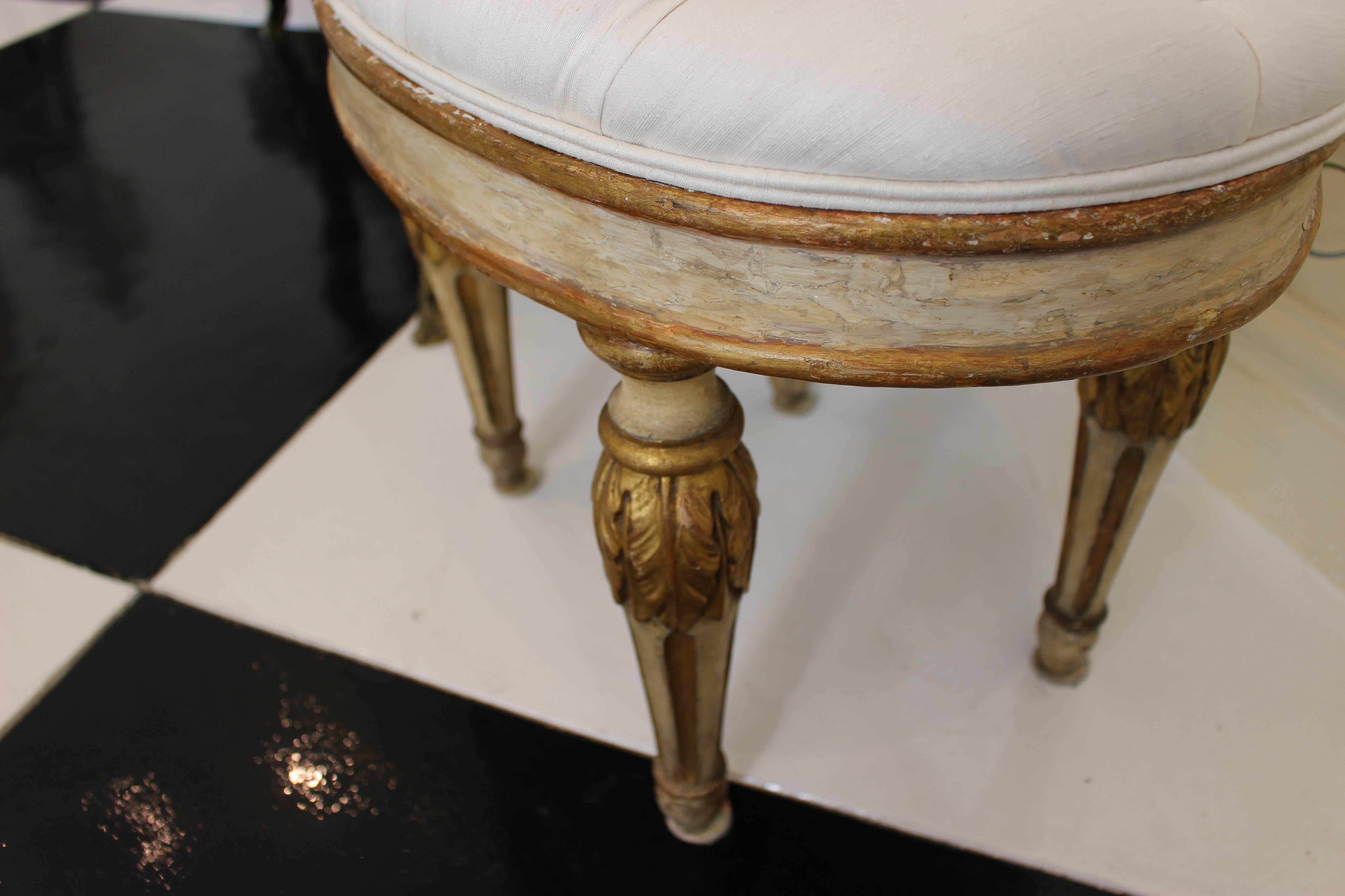 A pair of Italian Neoclassical period oval stools from the 18th century with white-painted bodies, parcel-gilt accents and upholstered seats. Born in the later years of the 18th century, each of this pair of Italian stools features an oval buttoned