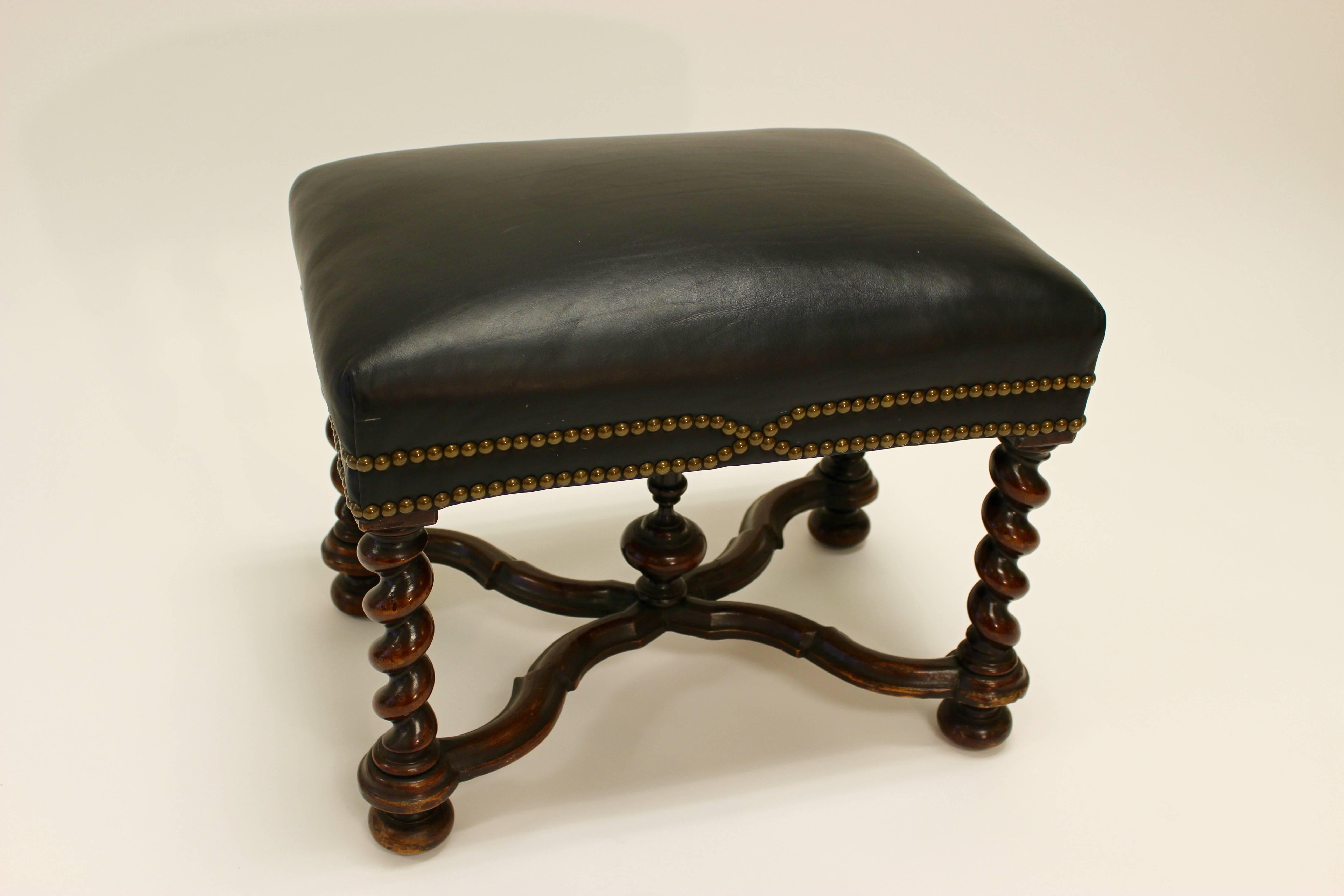 A William and Mary style leather upholstered bench from the 20th century with brass nailhead trim, barley twist base and cross stretcher. This walnut stool features a rectangular dark leather upholstered seat, raised on an exquisite base made of