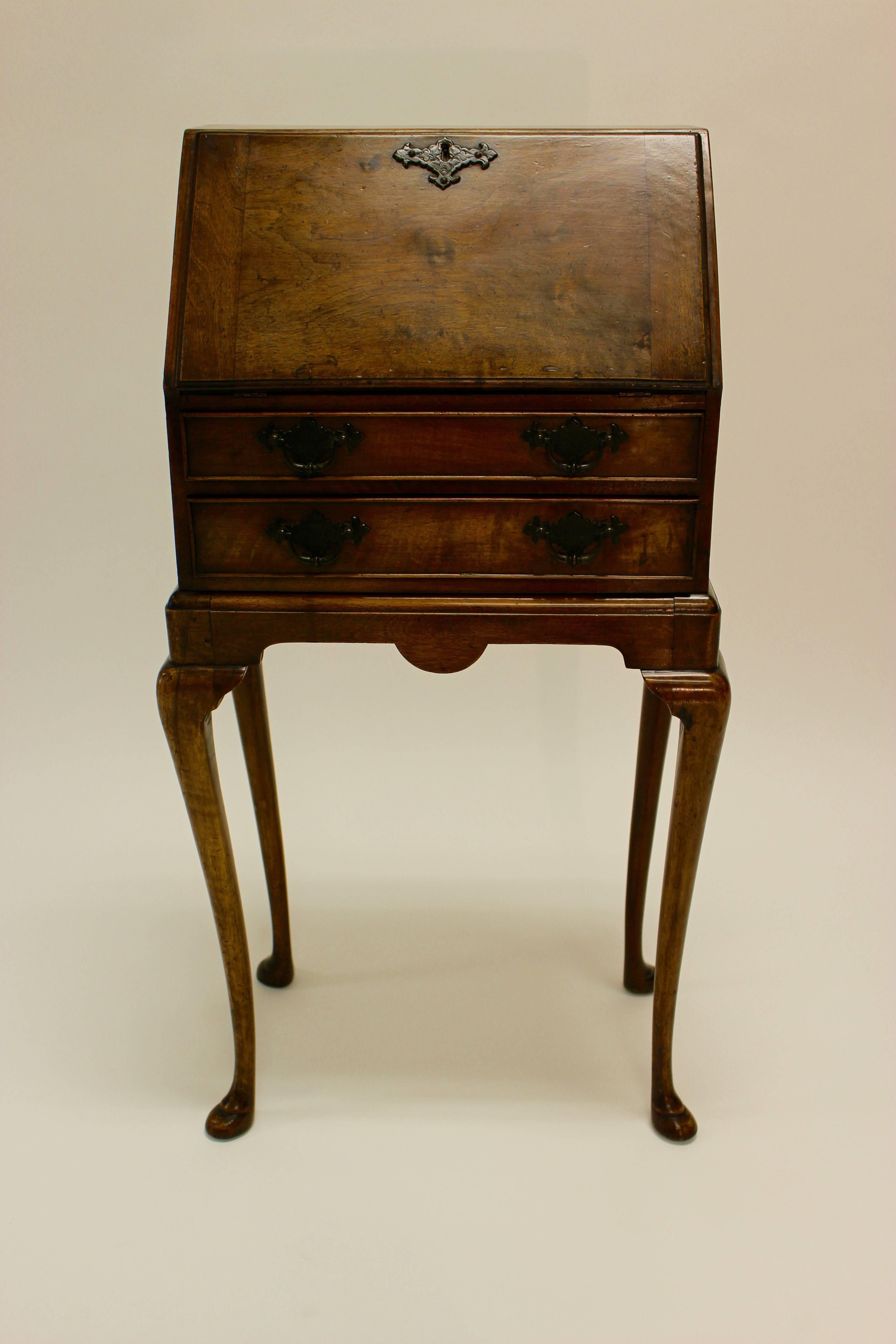 A late 19th century Queen Anne style small walnut mini slant front desk on stand resting on graceful cabriole legs ending in pad feet. The slant drop front, topped with a Chippendale bat-wings keyhole escutcheon nicely enhancing the figured walnut