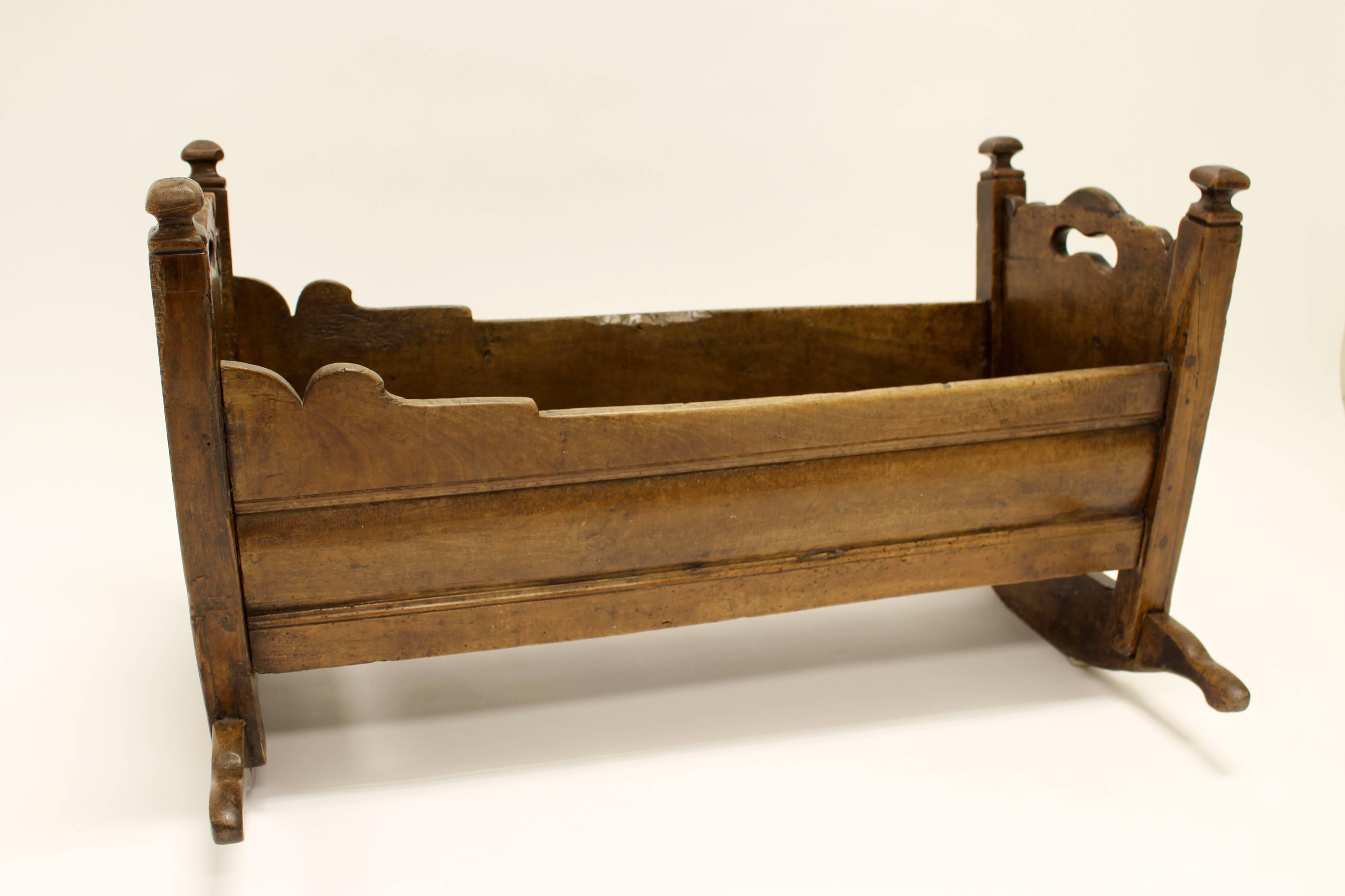 A unique and rare Italian walnut cradle signed. This example is formed in the traditional style with scalloped end boards surmounted by turret finials atop outstretched rockers. Lombardy, 18th century. 