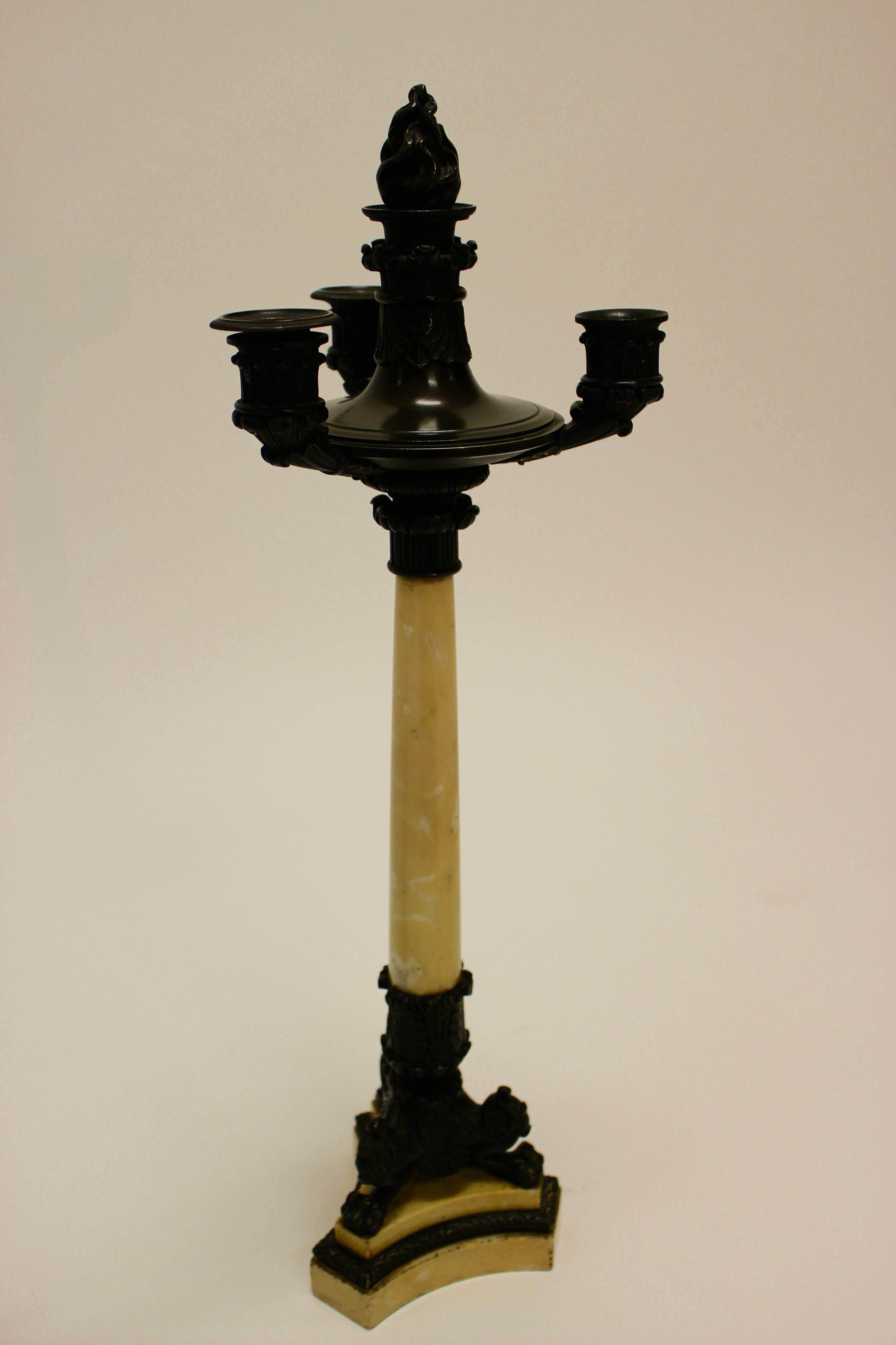 A late 19th century pair of matching triple candlesticks crafted of dark patinated brass and Siena marble. Each candlestick presents a tapering circular marble column supporting a brass circular plate issuing a central shaft. This shaft is topped