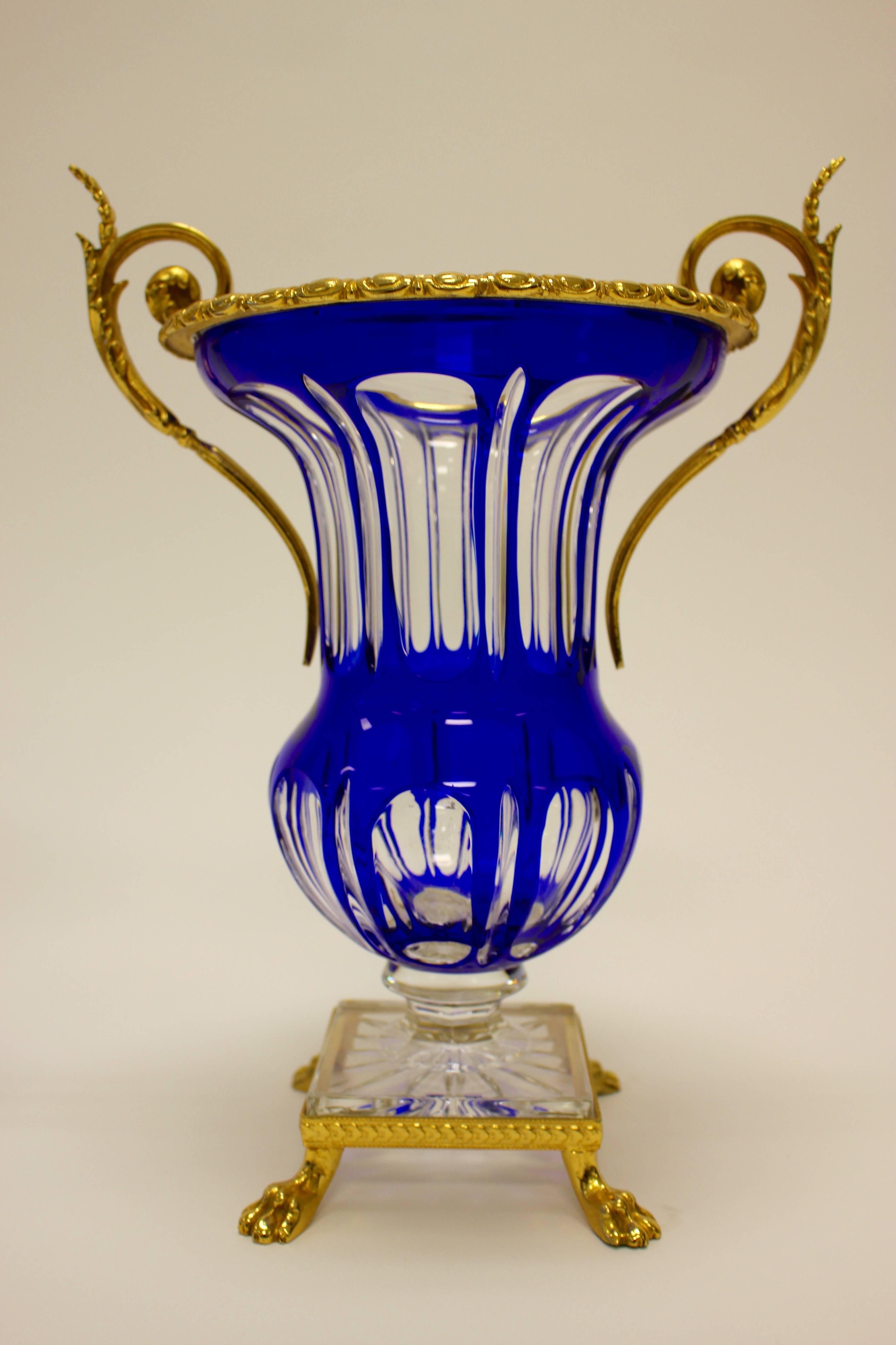 A pair of French gilt-metal clear crystal vases with cobalt-blue overlay from the mid-20th century. Each piece presents a waisted body over a swollen base atop a short baluster-shaped connector resting on a square pedestal. A beautiful cobalt-blue