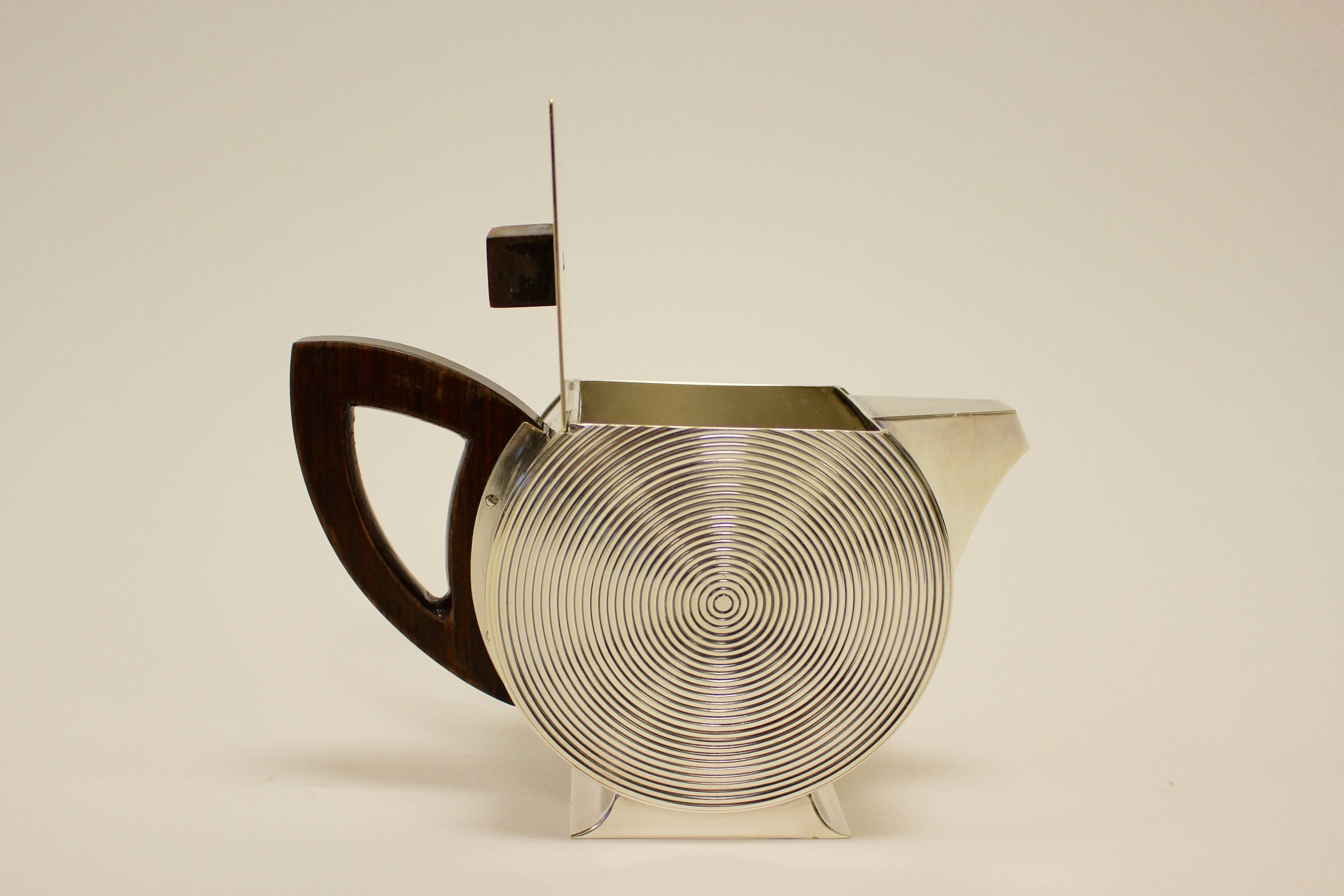 A French silver Art Deco five-piece tea and coffee set from the 20th century. The set comprises a teapot, a coffee pot, a creamer and a covered sugar bowl, all with flattened round bodies cut to the top with hinged covers, ear-shaped wooden handles