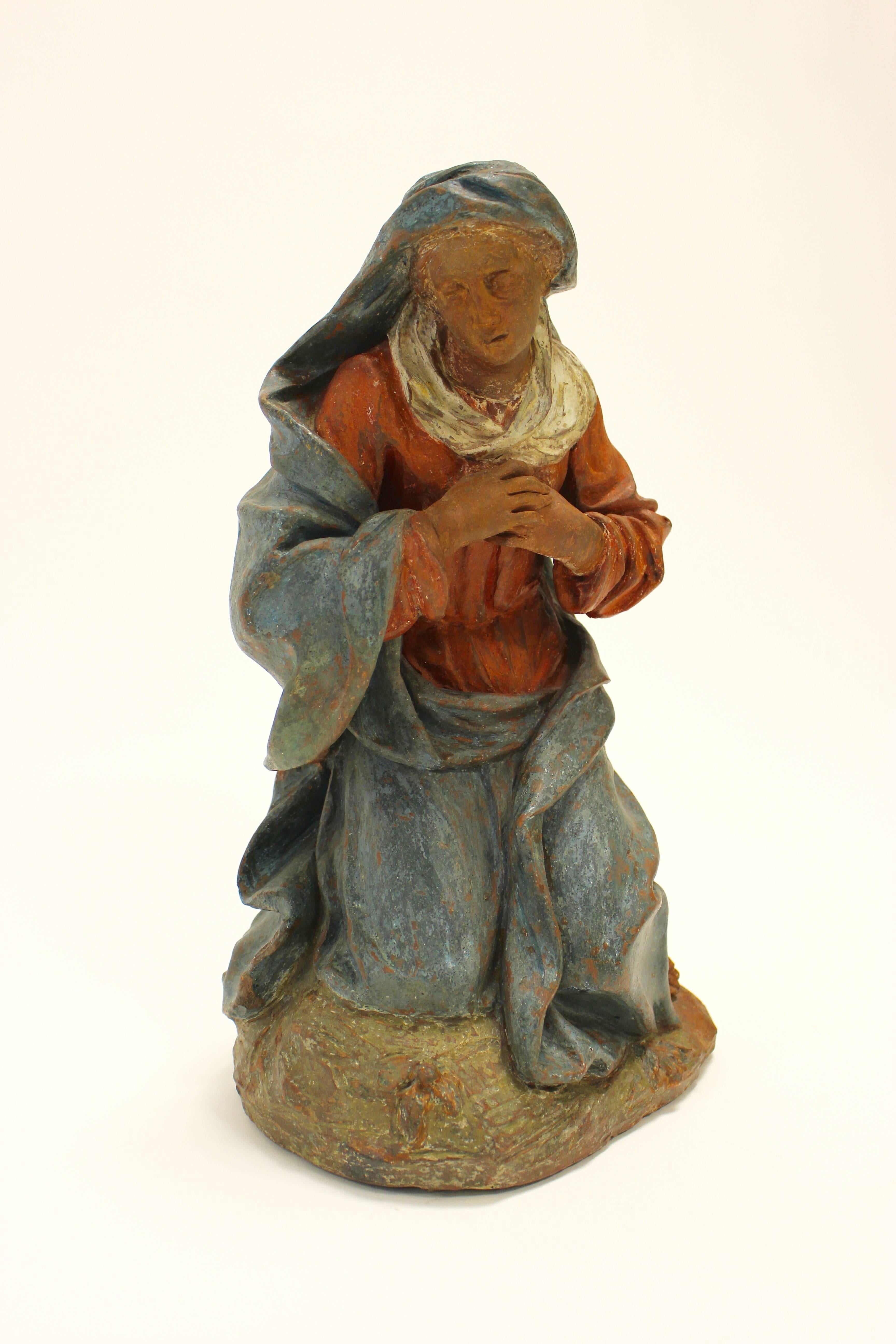 A 17th-18th century continental painted terracotta sculpture of a kneeling Virgin in the manner of Angolo di Poli. This exquisite terracotta sculpture features a poignant depiction of the Virgin Mary. The red and blue clothes that she is wearing