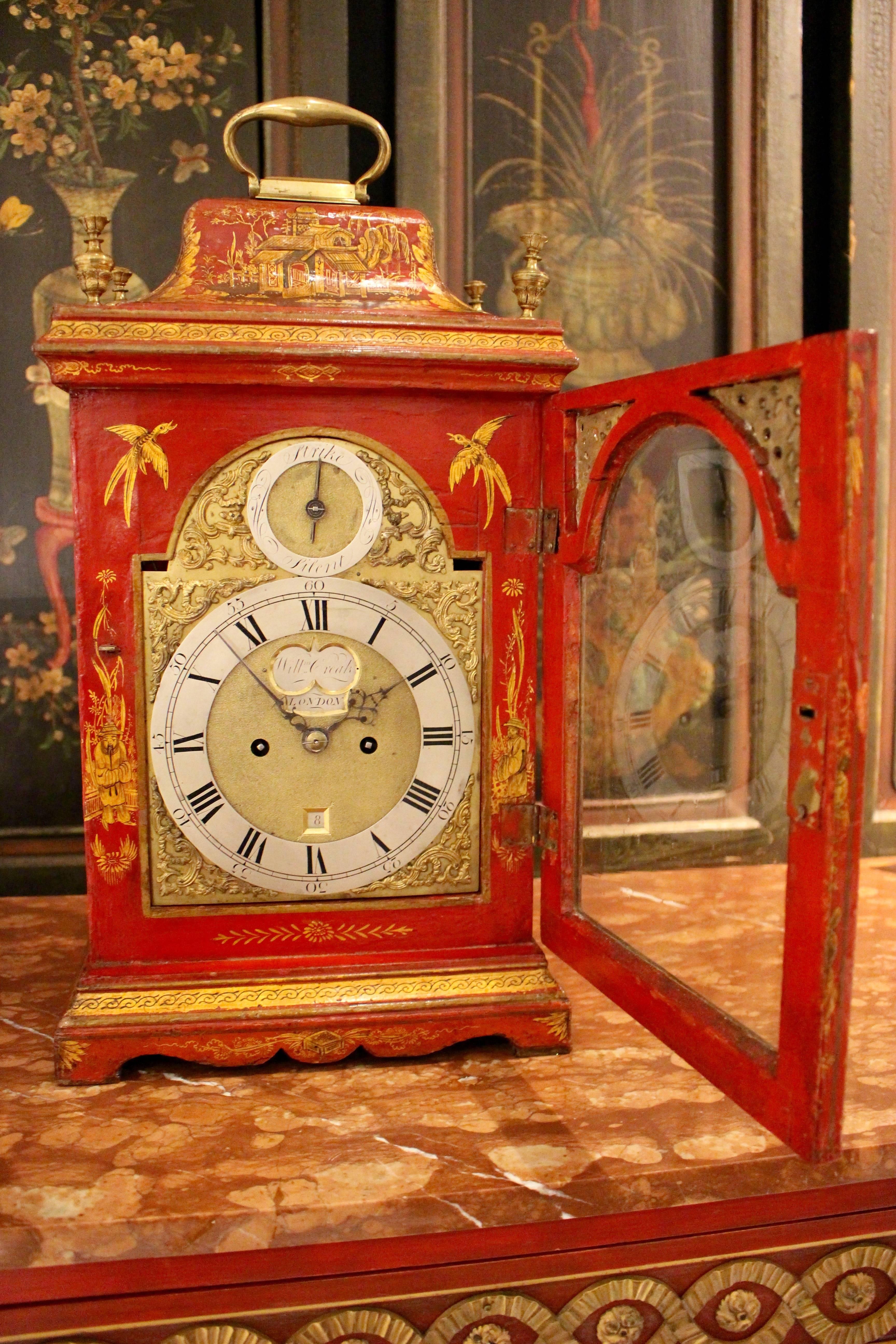 This English George II period 18th century table clock consists in a scarlet-japanned and parcel-gilt rectangular case with elaborate chinoiserie decoration and pierced frets to the sides. Resting on a molded base with a shaped apron and bracket