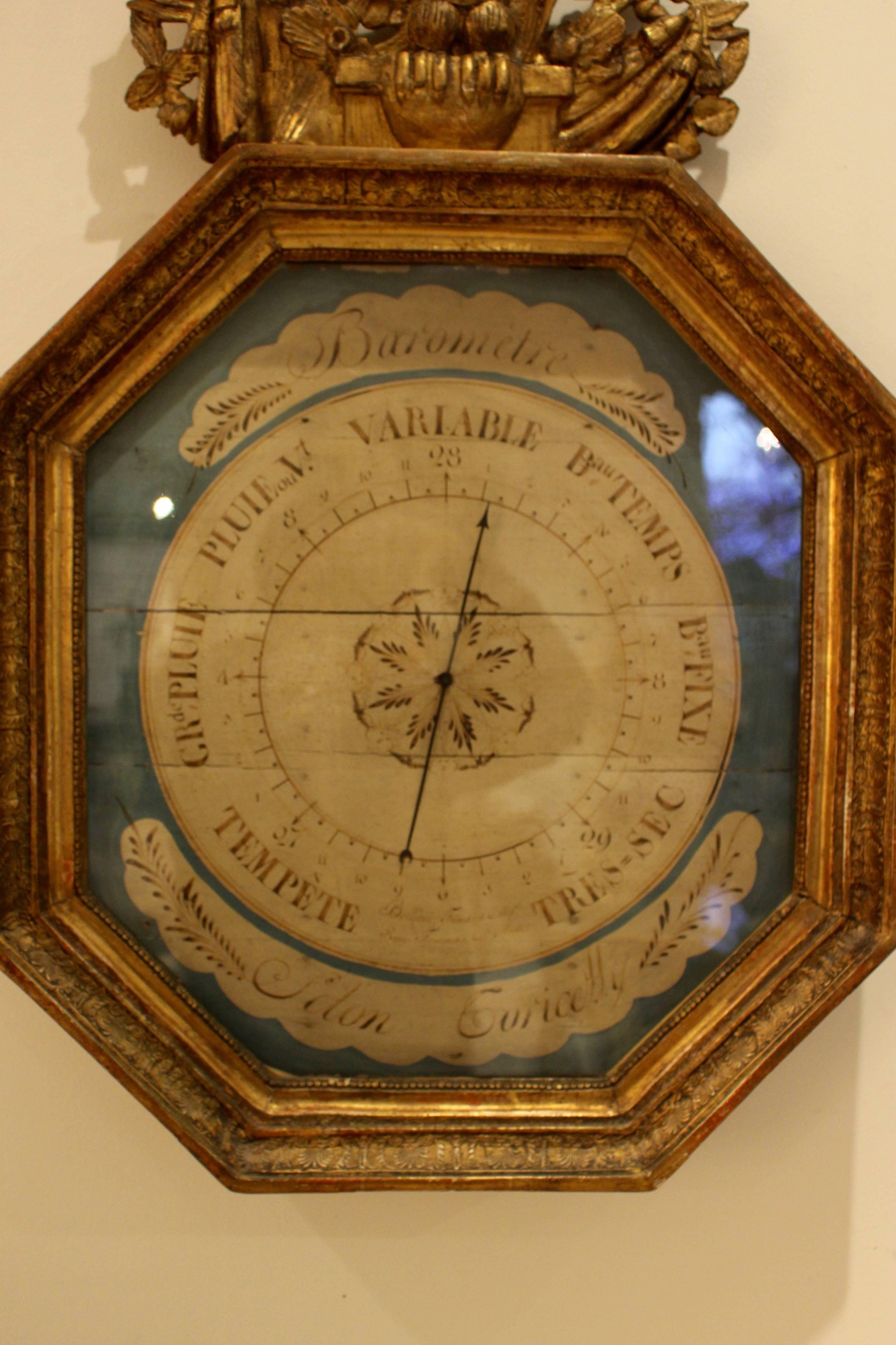 Französisches Barometer aus geschnitztem Goldholz aus der Restaurationszeit nach Toricelli. Das gemalte Zifferblatt auf blauem Grund ist mit einem Reigen geflügelter Putten und einer achtzackigen pflanzlichen Rose in der Mitte geschmückt, die eine