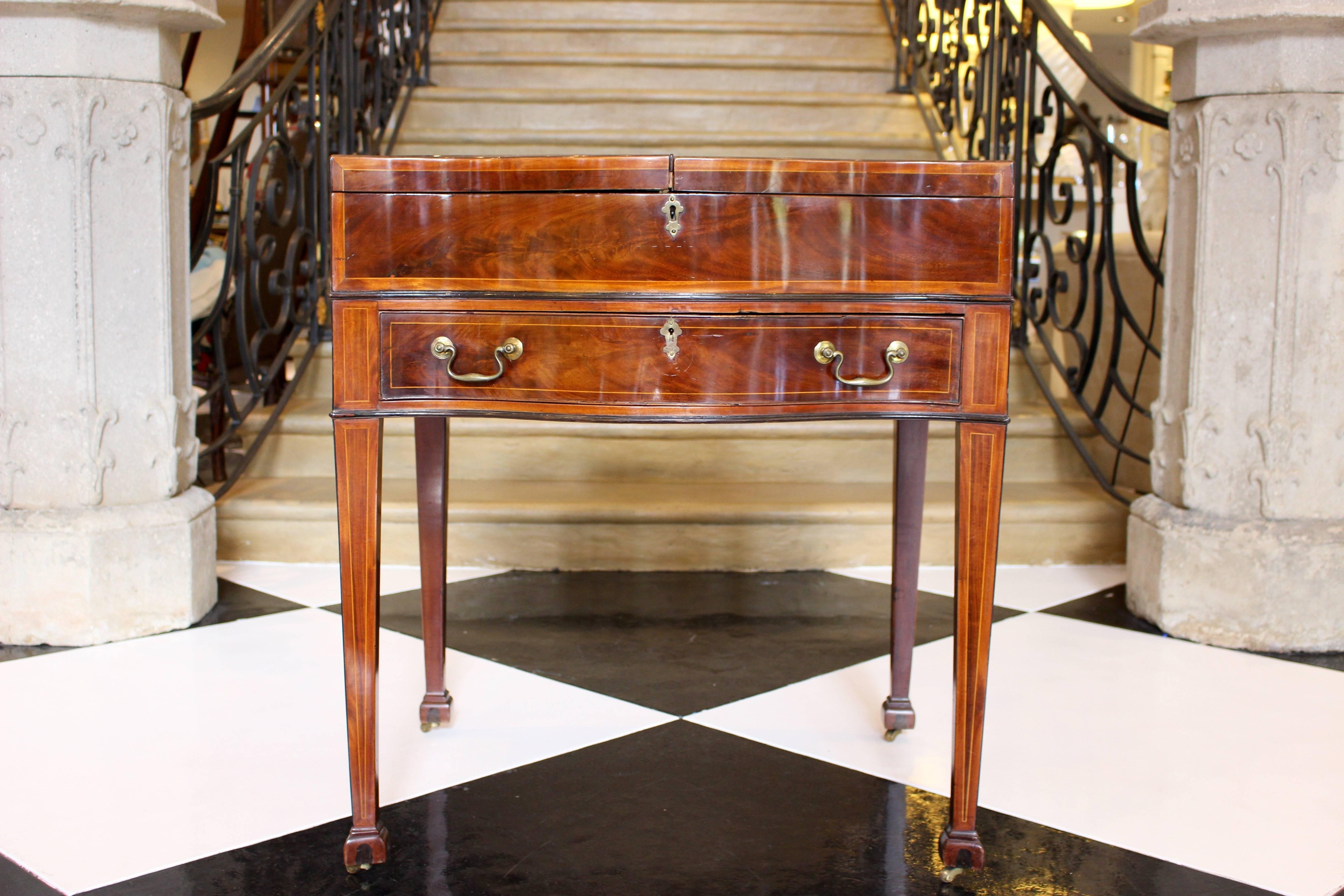 An English George III inlaid mahogany gentleman's dressing table from the last quarter of the 18th century. Raised on square tapering legs and brass casters, the serpentine case is composed of a single drawer with two brass swan neck handles