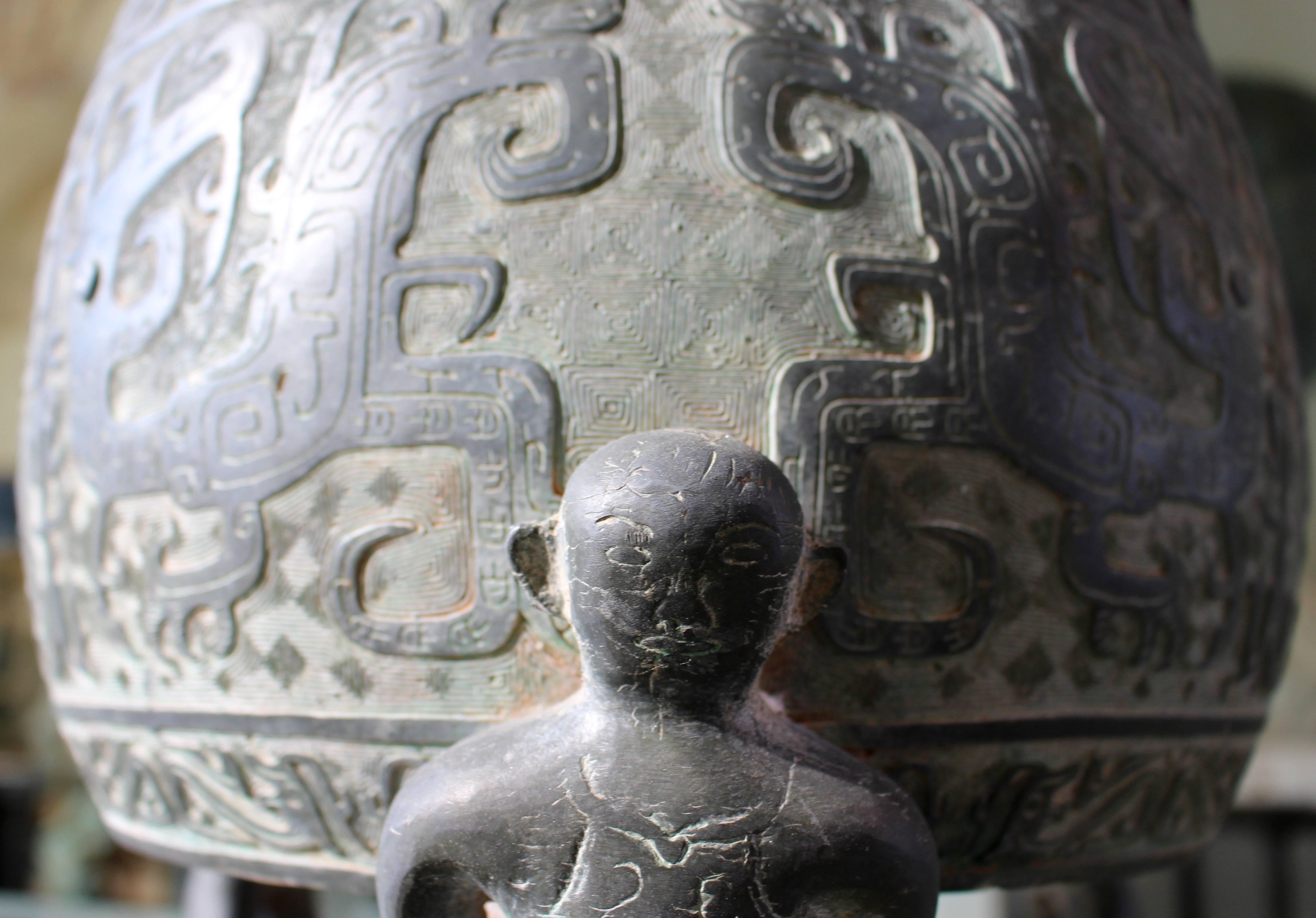 A Chinese four-legged barrel-form brass urn cast and engraved with archaistic decoration from the 20th century. The gently rounded sides are cast with the dispersed elements of two taotie masks, Archaistic auspicious beasts formed by a pair of