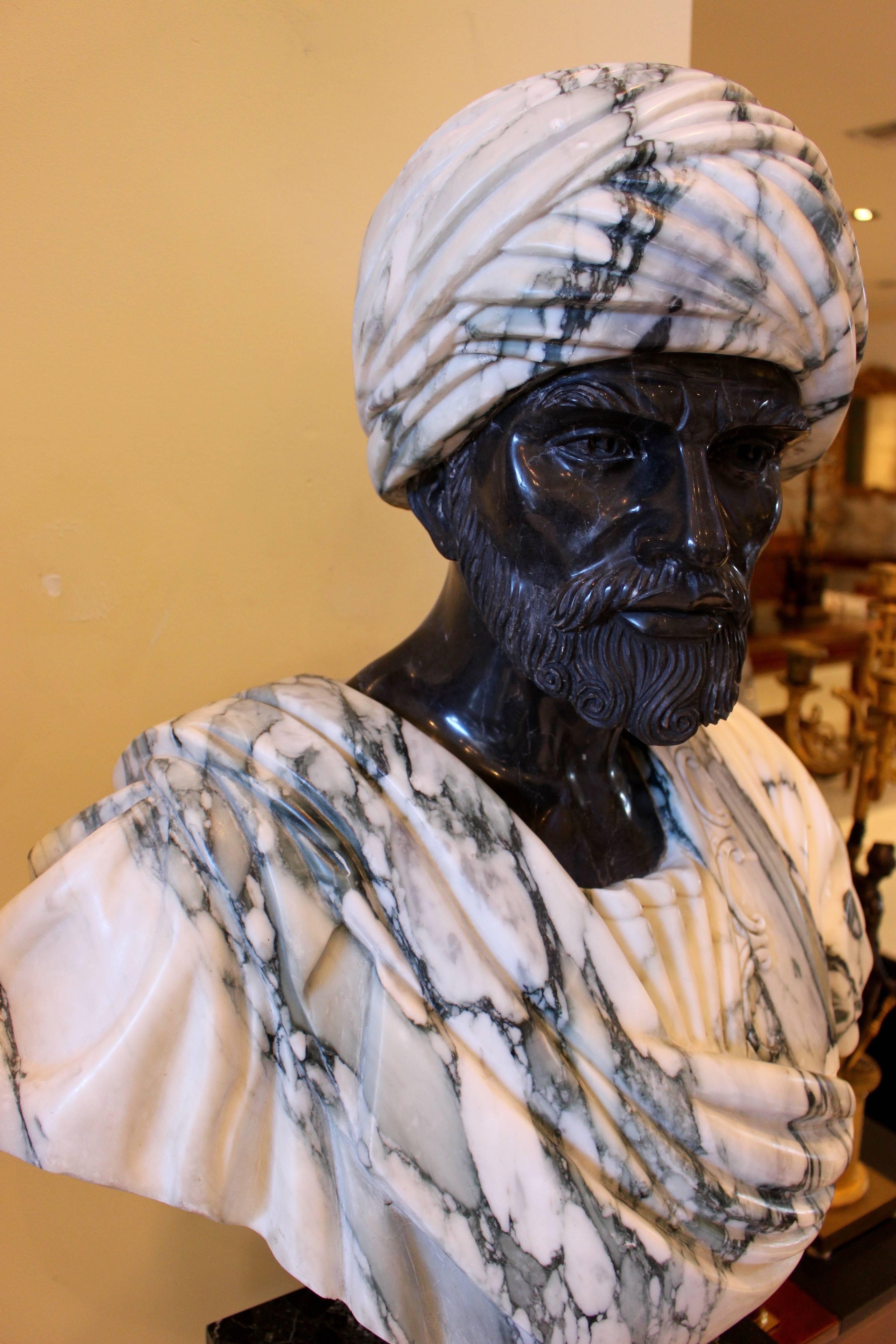 A carved grey and black marble draped bust from the 20th century raised by a mottled socle pedestal. This majestic draped bust shows a man already in old age with a stylized curly beard, the black marble face beautifully contrasting with the grey