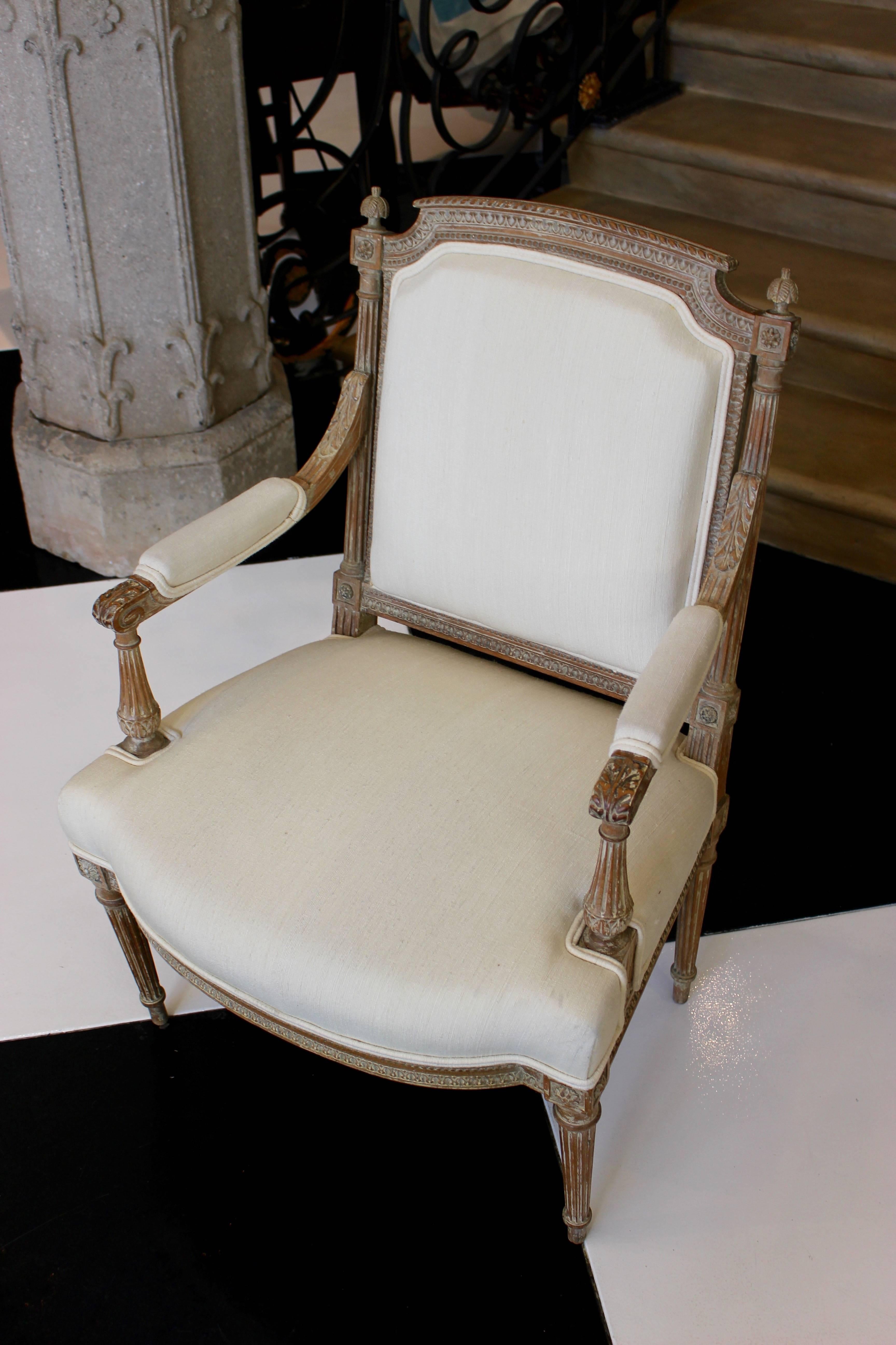 A French Louis XVI style carved wood fauteuil from the 19th century, with traces of original paint, foliage motifs, fluted legs and new upholstery. This exquisite French armchair features a rectangular back, adorned with a slightly arched upper