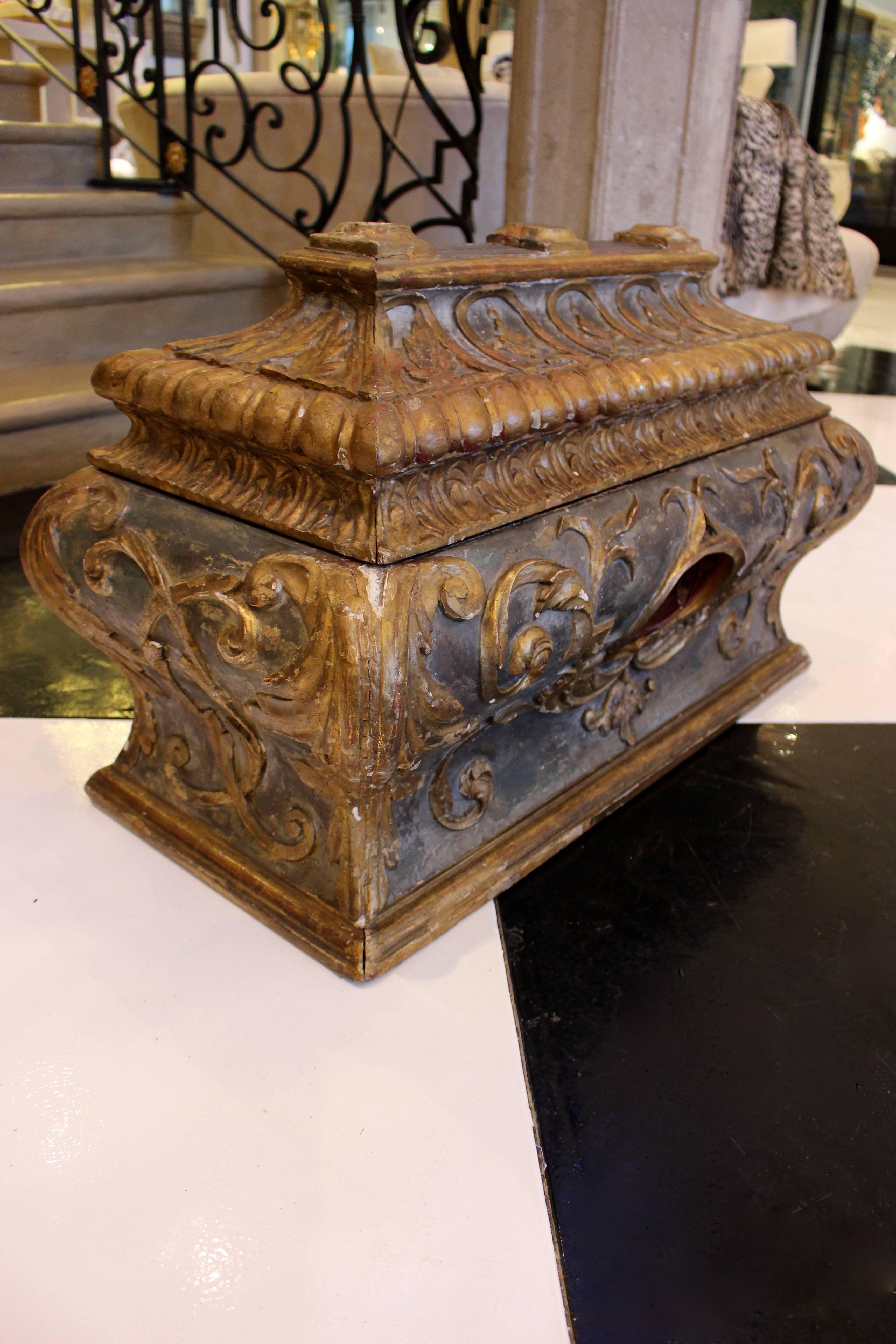 An Italian Rococo sarcophagus-shaped wooden chest of bombé rectangular form with richly carved gilt decoration on a distressed ebonized ground. The hinged pagoda top lid is skillfully carved with a frieze of urns in arches above a convex gadrooned