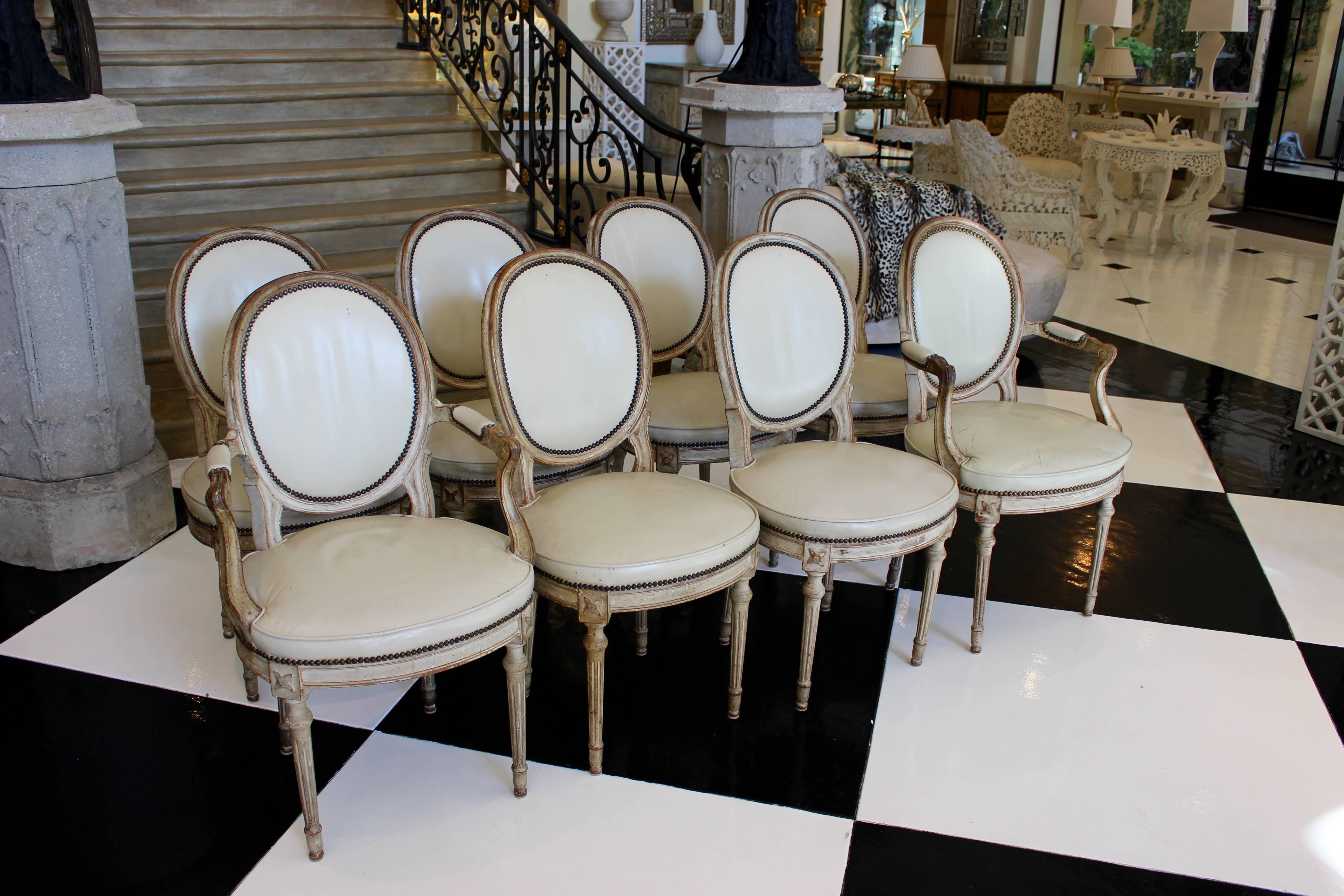 A set of eight French late Louis XVI style cream painted beech wood oval back dining room chairs from the early 19th century, with white leather upholstery. Born during the tumultuous period of the early 19th century after the fall of the Ancien