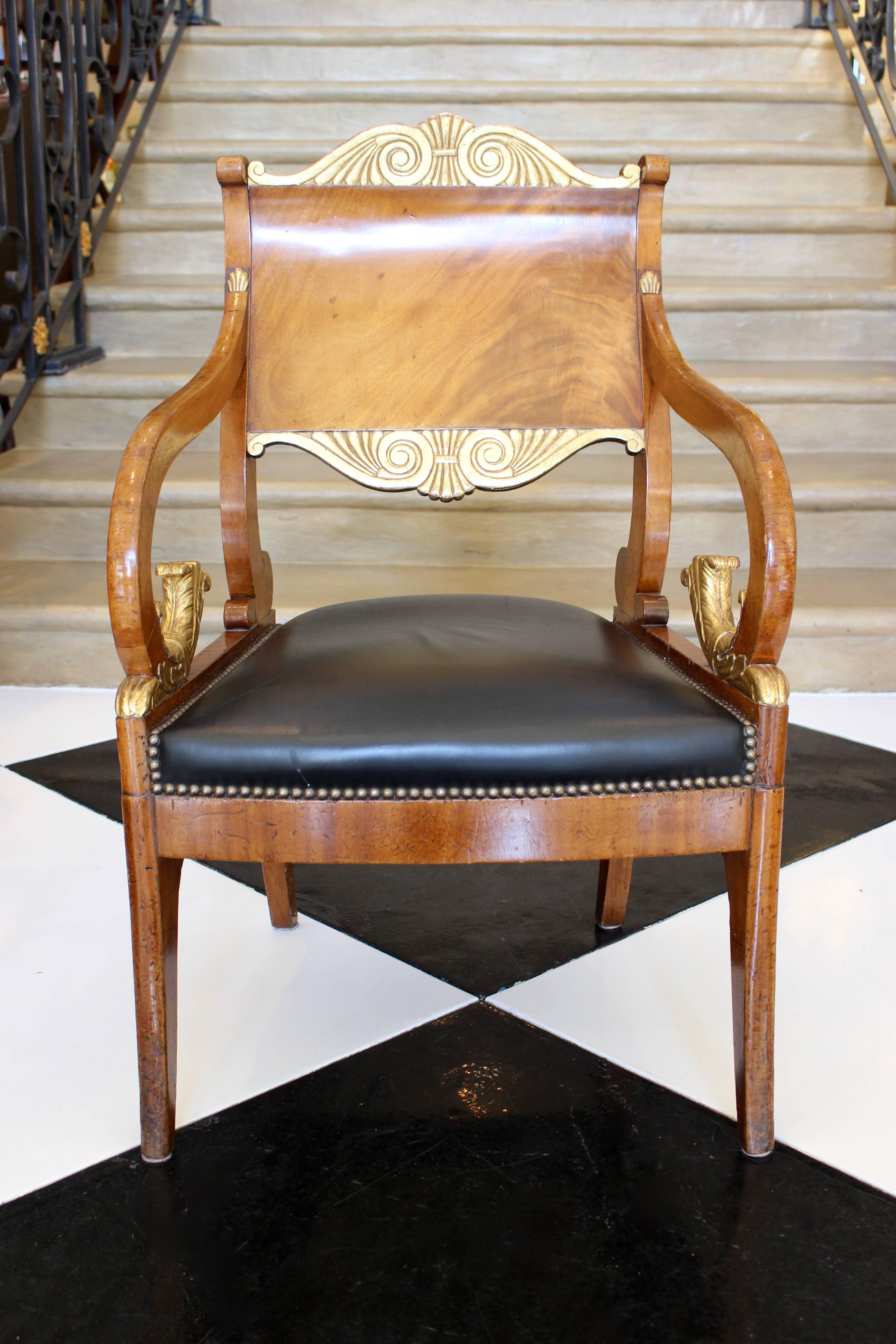 A pair of Russian Neoclassical period mahogany parcel-gilt armchairs from the second half of the 18th century, with palmette motifs, black upholstered seats with nailhead trims and scrolled foliage. Each of this exquisite pair of Russian armchairs