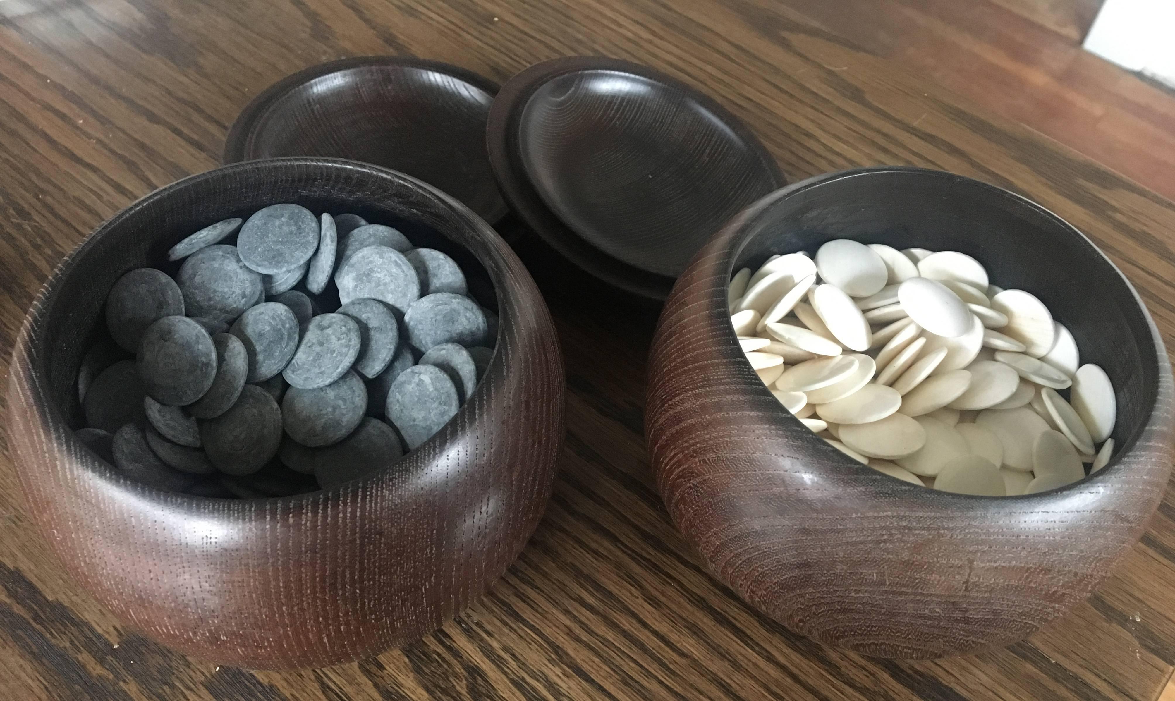 Beautiful set of Japanese go game playing chips made from shell and slate. Both chips are house in a simple wooden bowl with lid. Purchased at Takashimaya. 

This game was invented in ancient China more than 2,500 years ago, and is the oldest