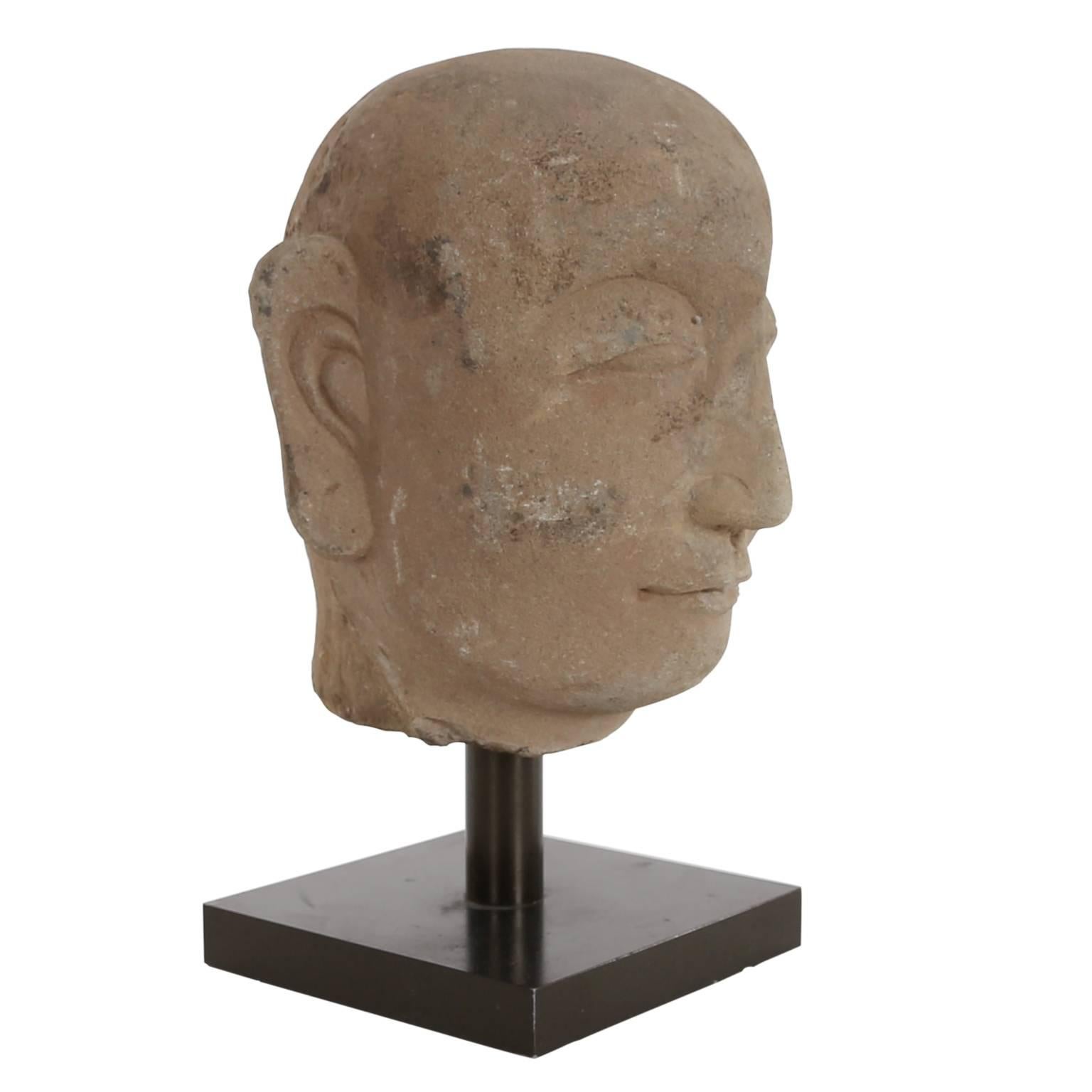 A Chinese carved stone head, with stylized features and a serene expression, Qing dynasty, on a modern stand.
Provenance: The collection of the Late John Walden (1925-2013).
 