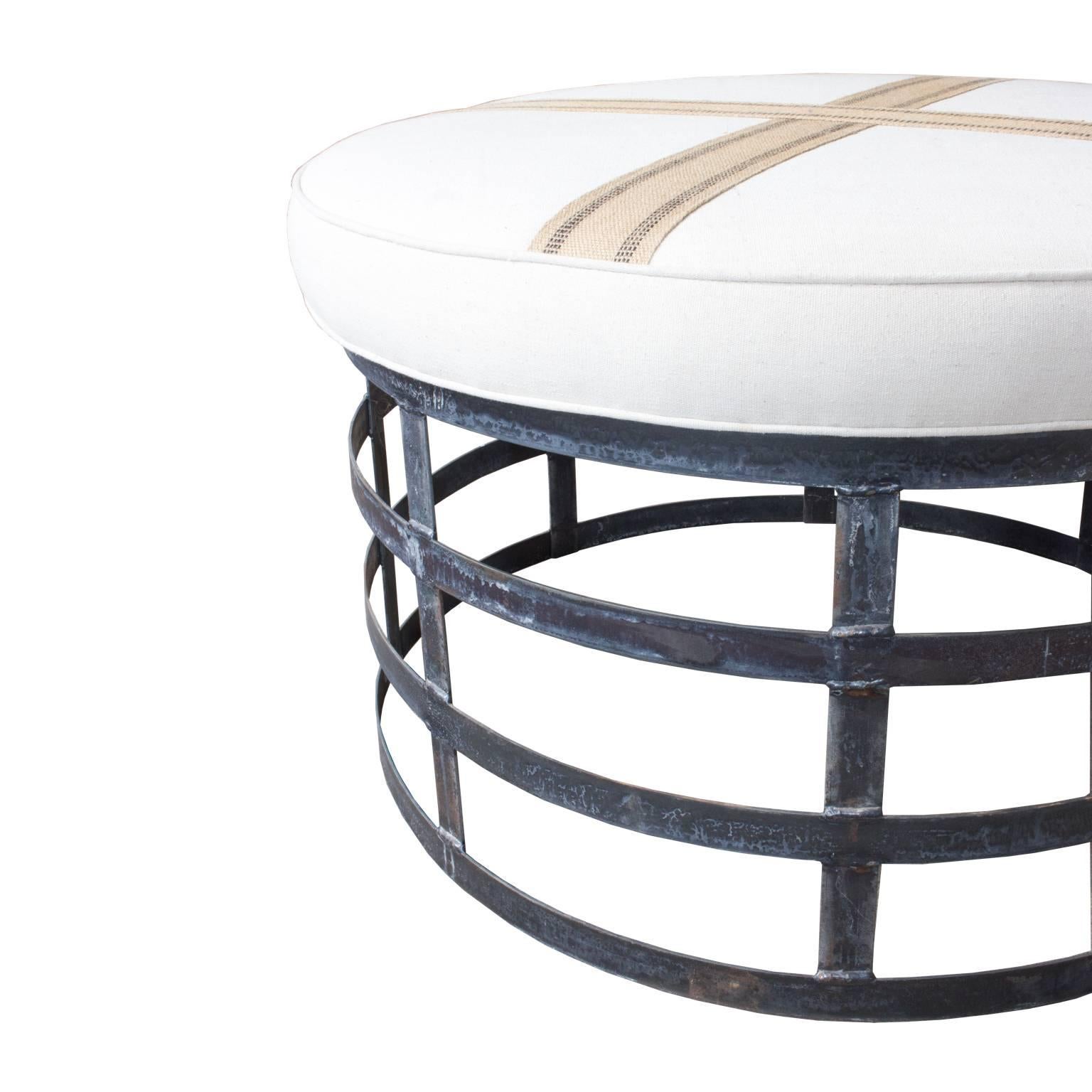 This large, industrial-inspired ottoman was fabricated with an open, steel frame. The top of the ottoman is upholstered in cotton linen and accented with gorgeous burlap ribbon in a cross pattern. This ottoman is just above coffee-table height, so
