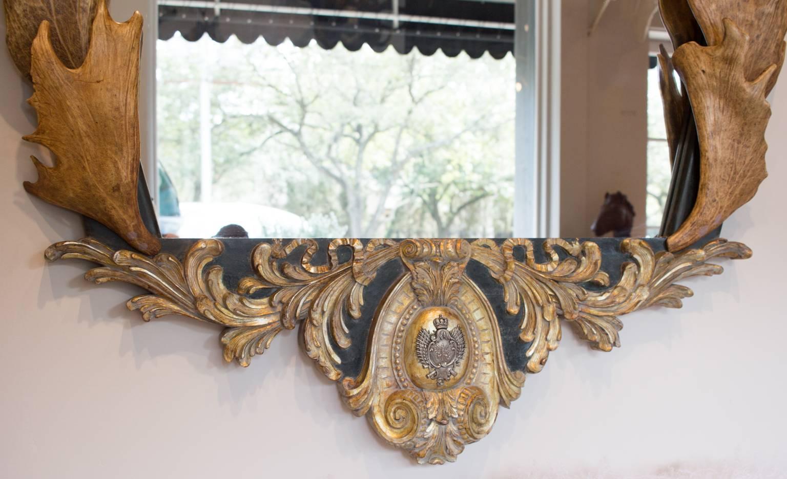 This is a stunning wall mirror with beautiful hand-carved details, including a lifesize, hand-carved roe head with antique roe antlers at the top, antique fallow antlers along the sides, and an original Prussian gorget of the Light of the Calvary of