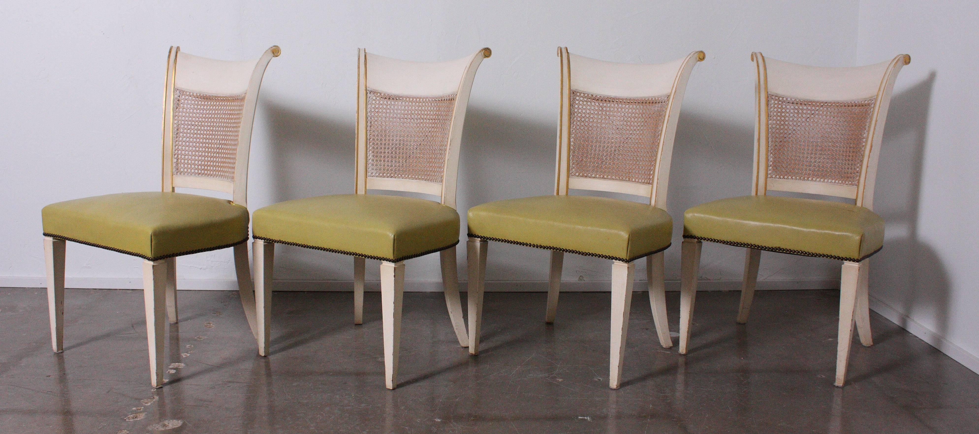 Set of four Hollywood Regency Klismos dining chairs from Baker. Chairs upholstered in original leather with cane backs and wonderful gold detailing.