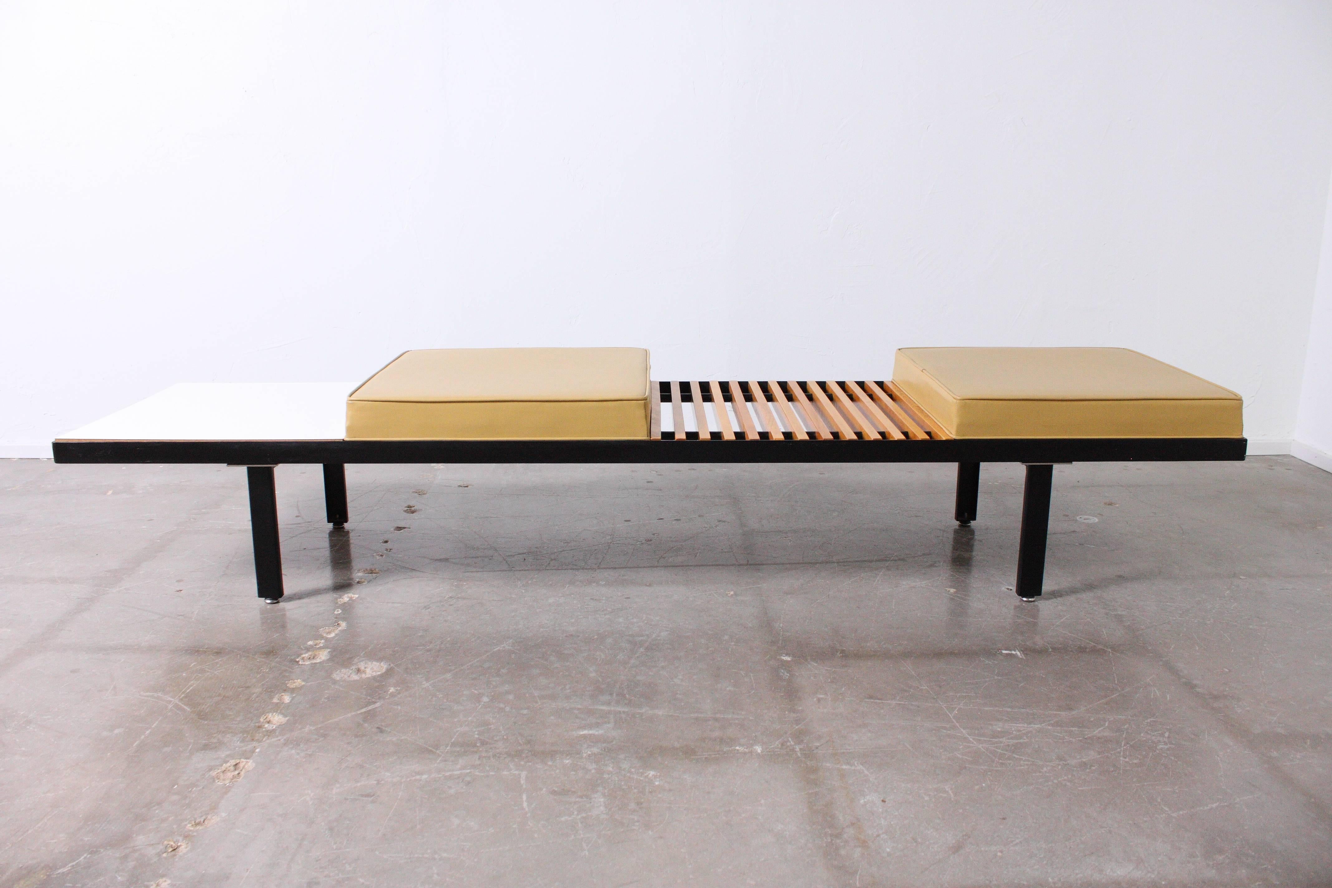 Long steel multi surface bench with two cushions, one wood slated table area and one Formica style table area.