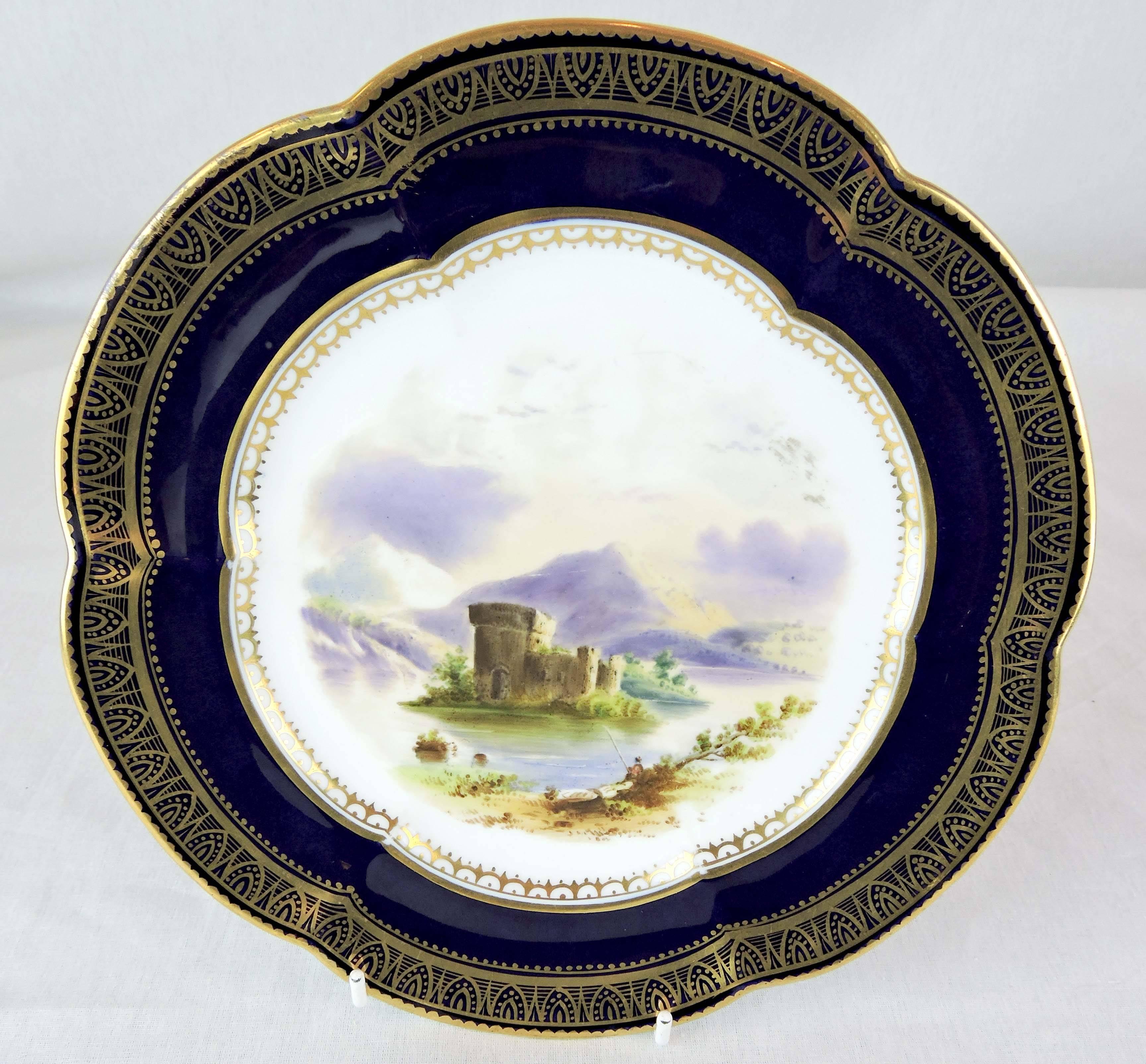 This is a pair of decorative porcelain plates by Spode, with scalloped, cobalt blue rims and hand-applied, architectural, gilt borders. Restrained, dentelle, gilt trim also frames the central paintings.

The plates depict two different vistas: