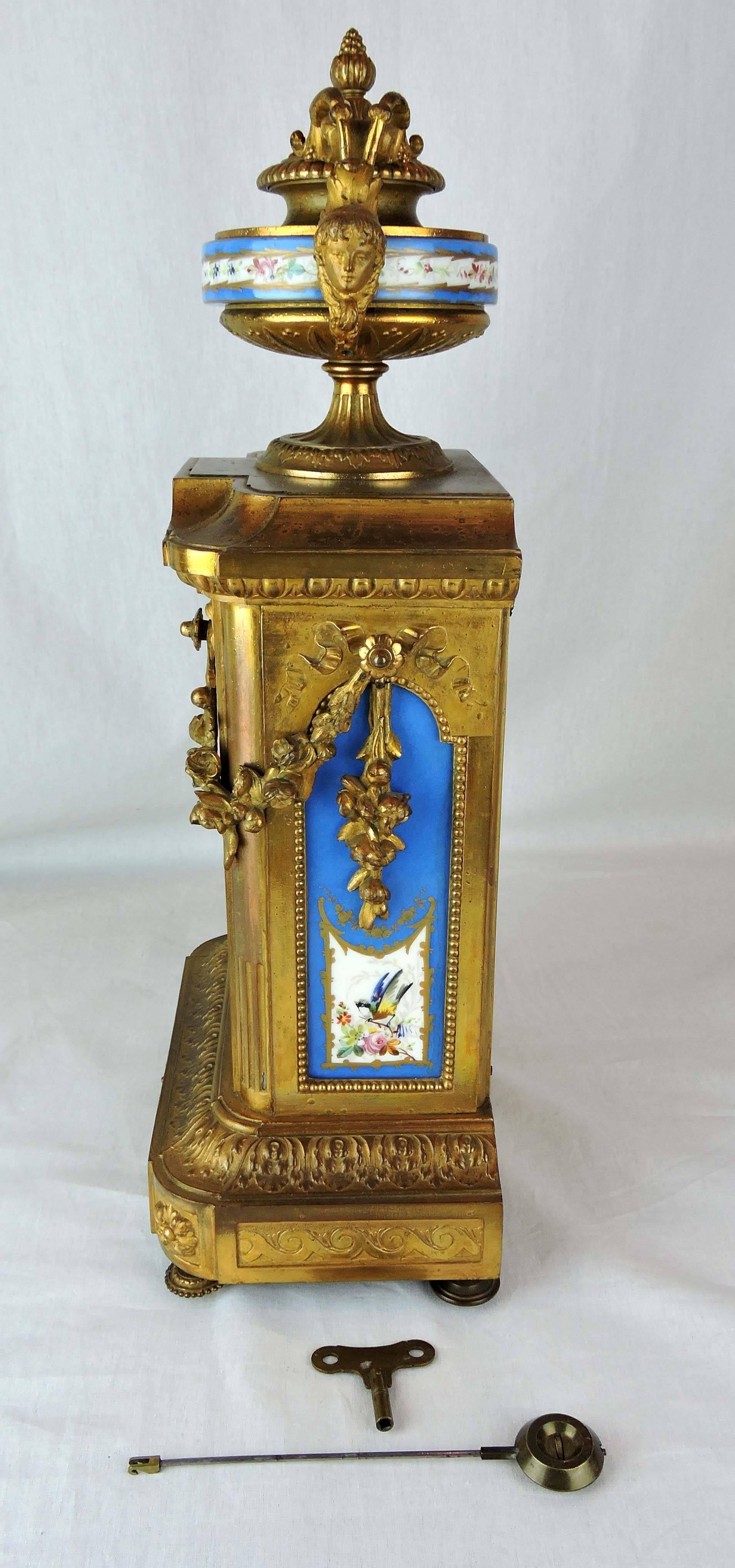 We offer a French 19th century, elongated, rectangular, gilt ormolu mantle clock with decorative porcelain panels.

The time piece is surmounted by a squat, cylindrical, lidded, neoclassical urn with figural handles trailing floral garlands and,
