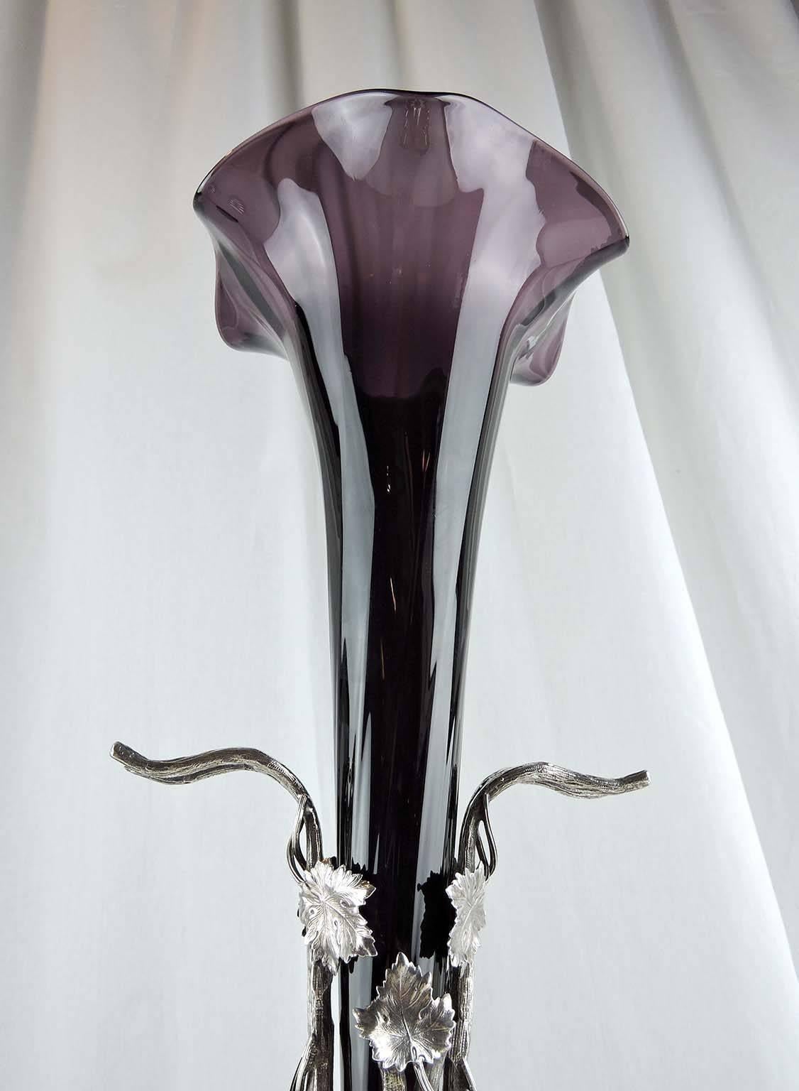 This beautiful epergne consists of a fluted, conical, amethyst glass center vase, held in place in a raised, silver plate holder of grapes, vines and leaves. Stylized implement hooks formed of 
