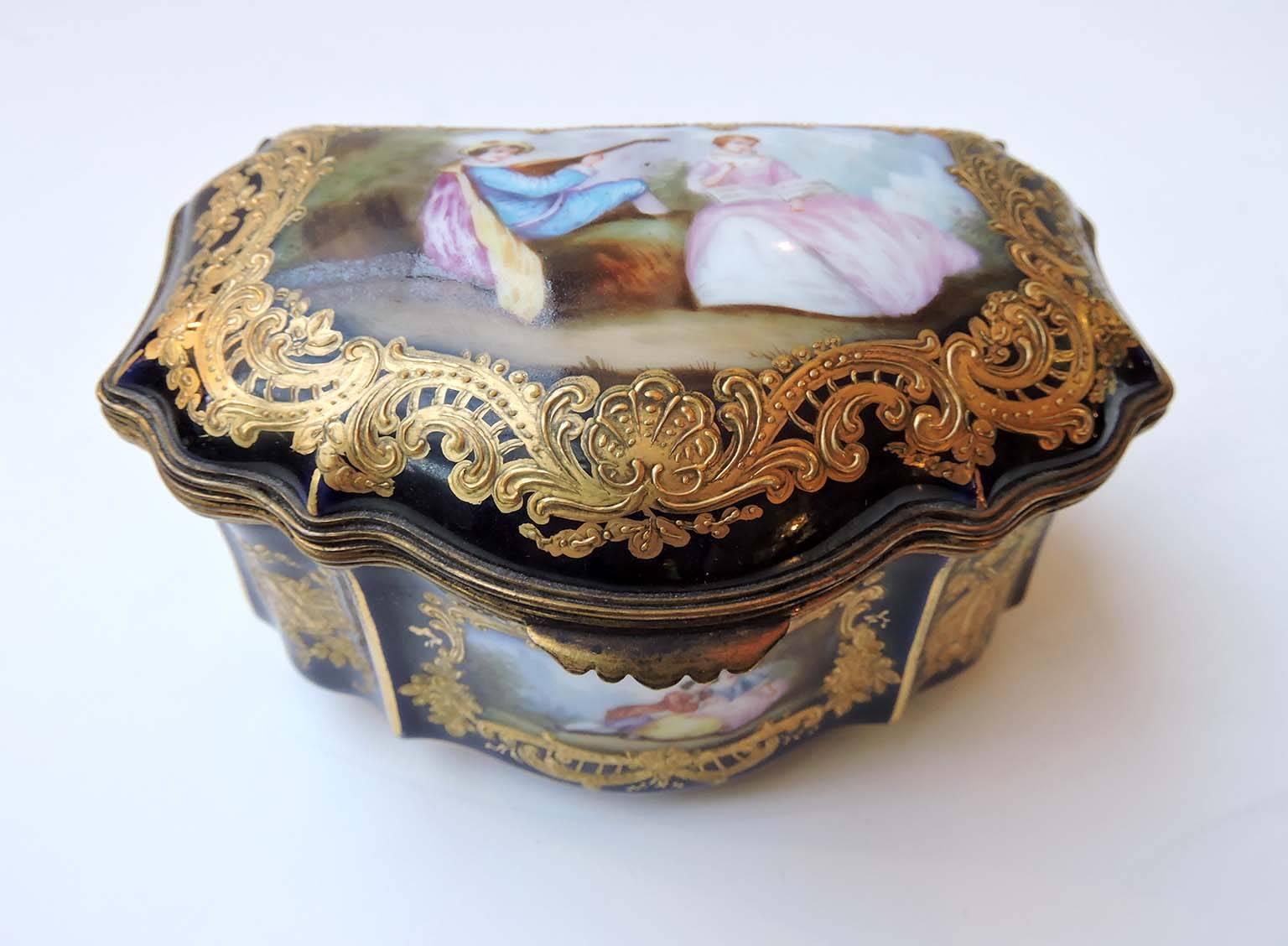 This is a fine cobalt blue porcelain trinket box with hinged cover and ormolu mounts. 

The domed lid features a large cartouche: A figural study of lovers in a pastoral setting. The painting is richly framed with raised, foliate, and gadroon