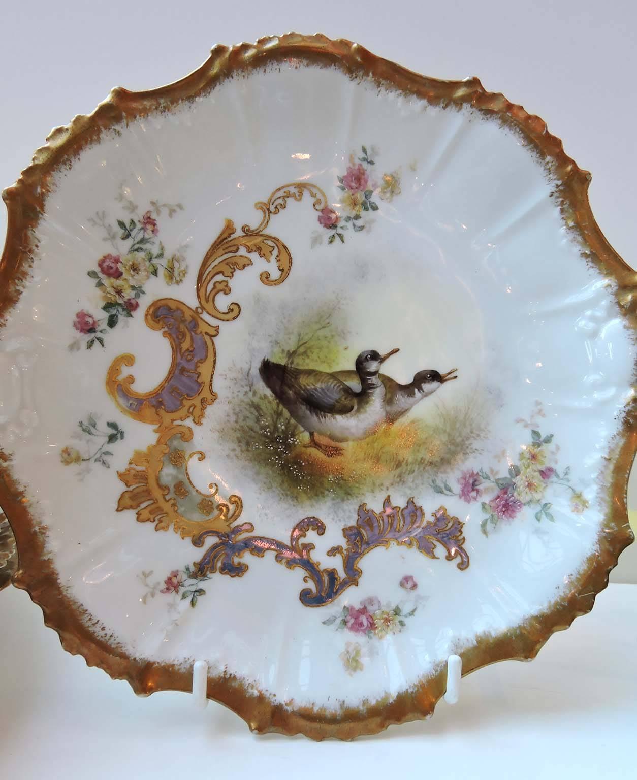 This very attractive set of Limoges game plates has raised, fluted and scalloped rims embellished with hand-applied gilt. 

The centre of each plate depicts a pair of game birds: Woodcocks, grouse, ducks and pheasants in a woodland setting,