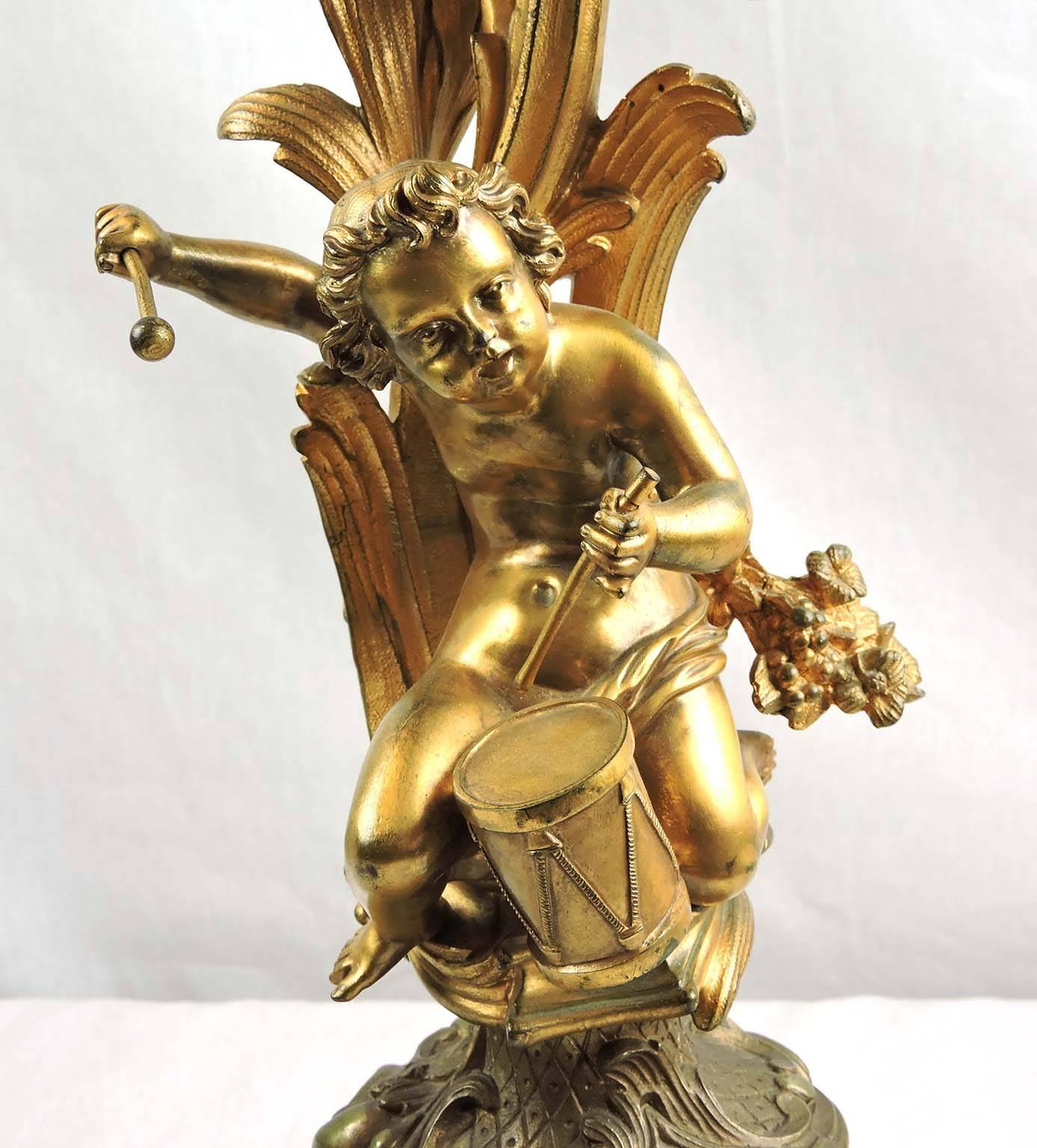 A pair of centre, thread-mounted gilt bronze Rococo candelabra, the foliate curvilinear shafts each ornamented with a seated cupid musician and sprays of flowers and issuing six, torsed, foliate arms, topped with goblet-shaped candleholders,