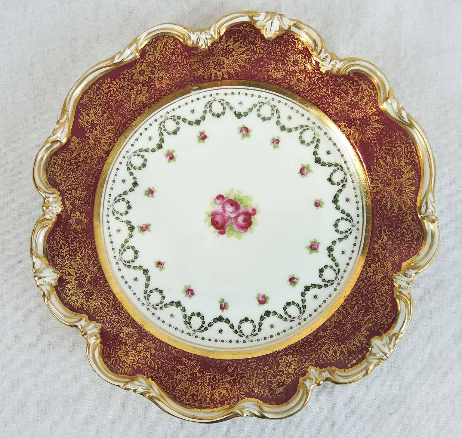 A lovely set of 12 dessert dishes, each with a white, gilt trimmed, scalloped foliate and shell edge surrounding a flat, crimson rim, overlaid with fine floral gilt.

The gold banded centres have classical green laurel wreaths and swags, with an