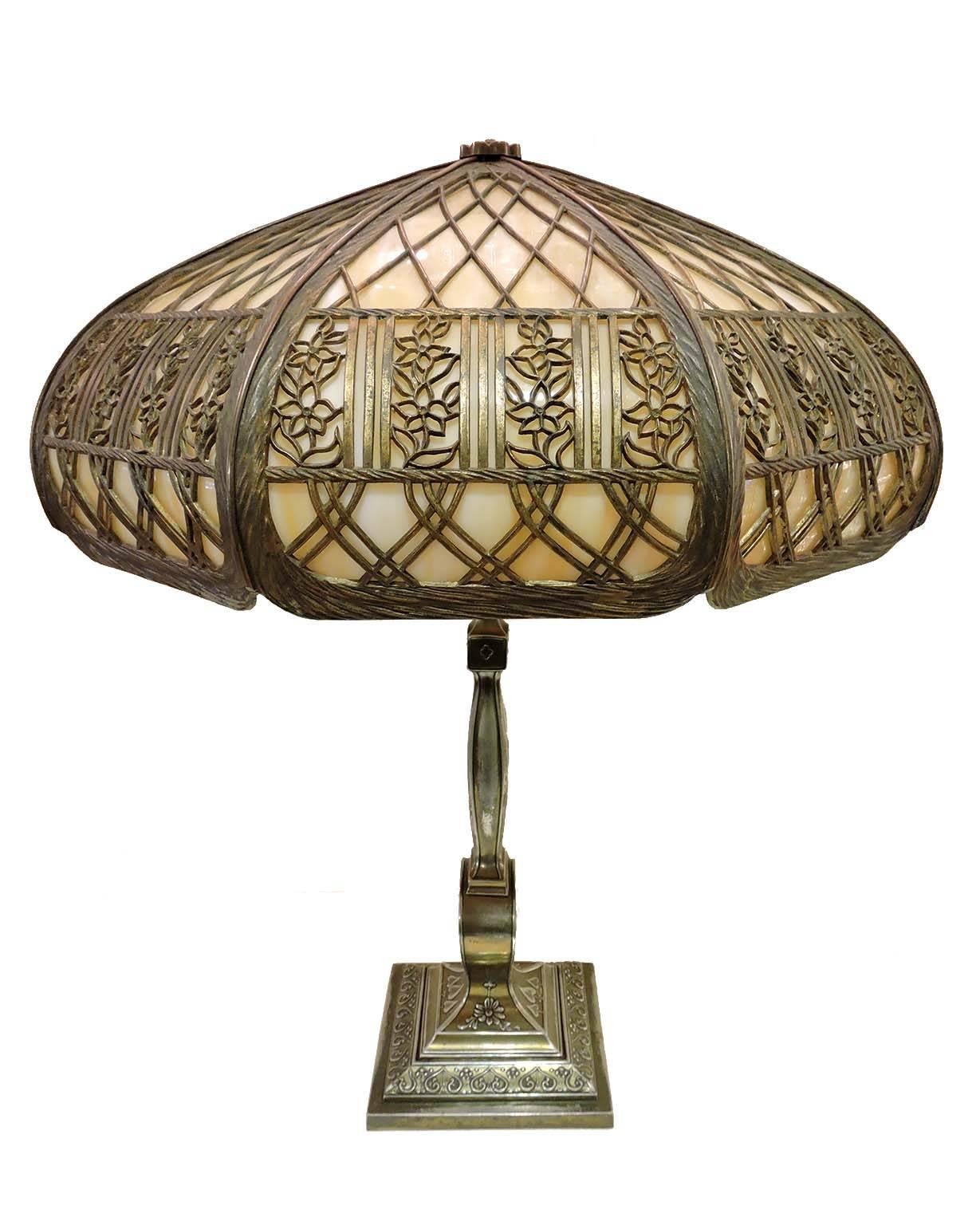 This beautiful electric turn of the century electric lamp features a Pairpoint base of patinated metal, consisting of square foot beneath a baluster post, both with raised and impressed foliate and geometric decoration. The post is topped with two
