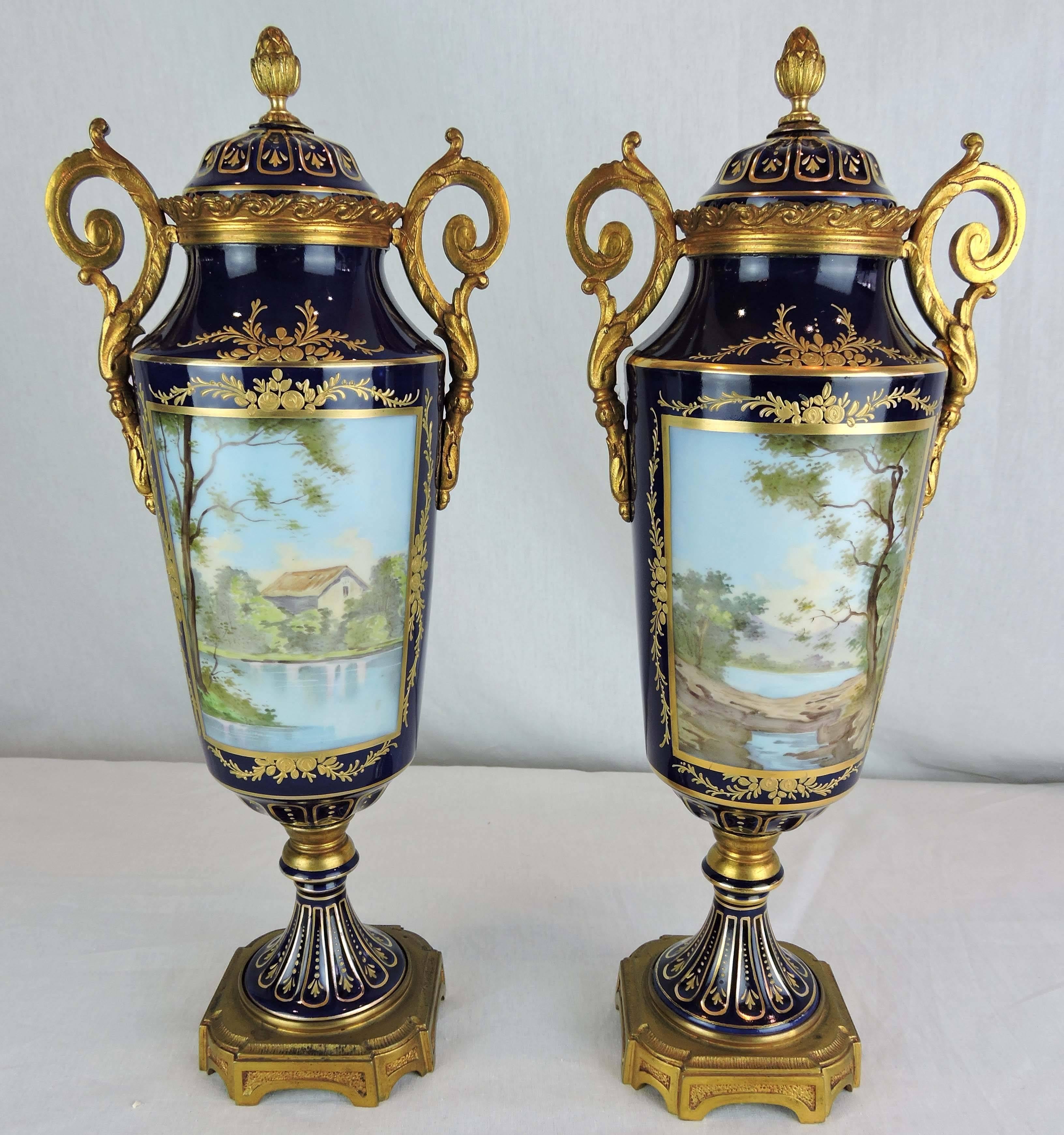 This pair of elongated baluster urns with inset pedestal feet, is decorated in the manner of Sevres, with cobalt blue bodies overlaid with ornate linear and foliate gilt, circa 1890.

Panelled, dome-shaped lids, crowned with bronze finials are