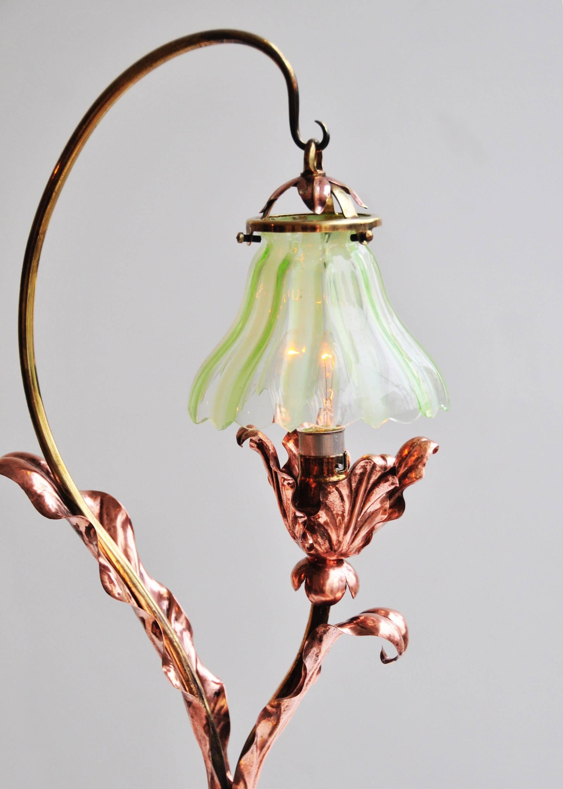 Sheet and tubular brass stem and base on ball feet, with copper leaf decoration and original Vaseline glass hanging shade, base stamped BENSON.

England, circa 1898.