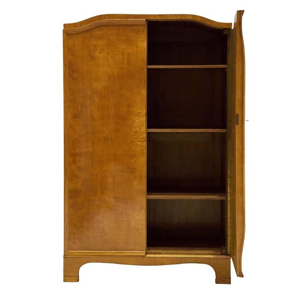 Veneered birch of exceptional figure and color with unusual bowed inlaid doors with lock and key. One has three shelves while the other has hanging space below a top shelf.