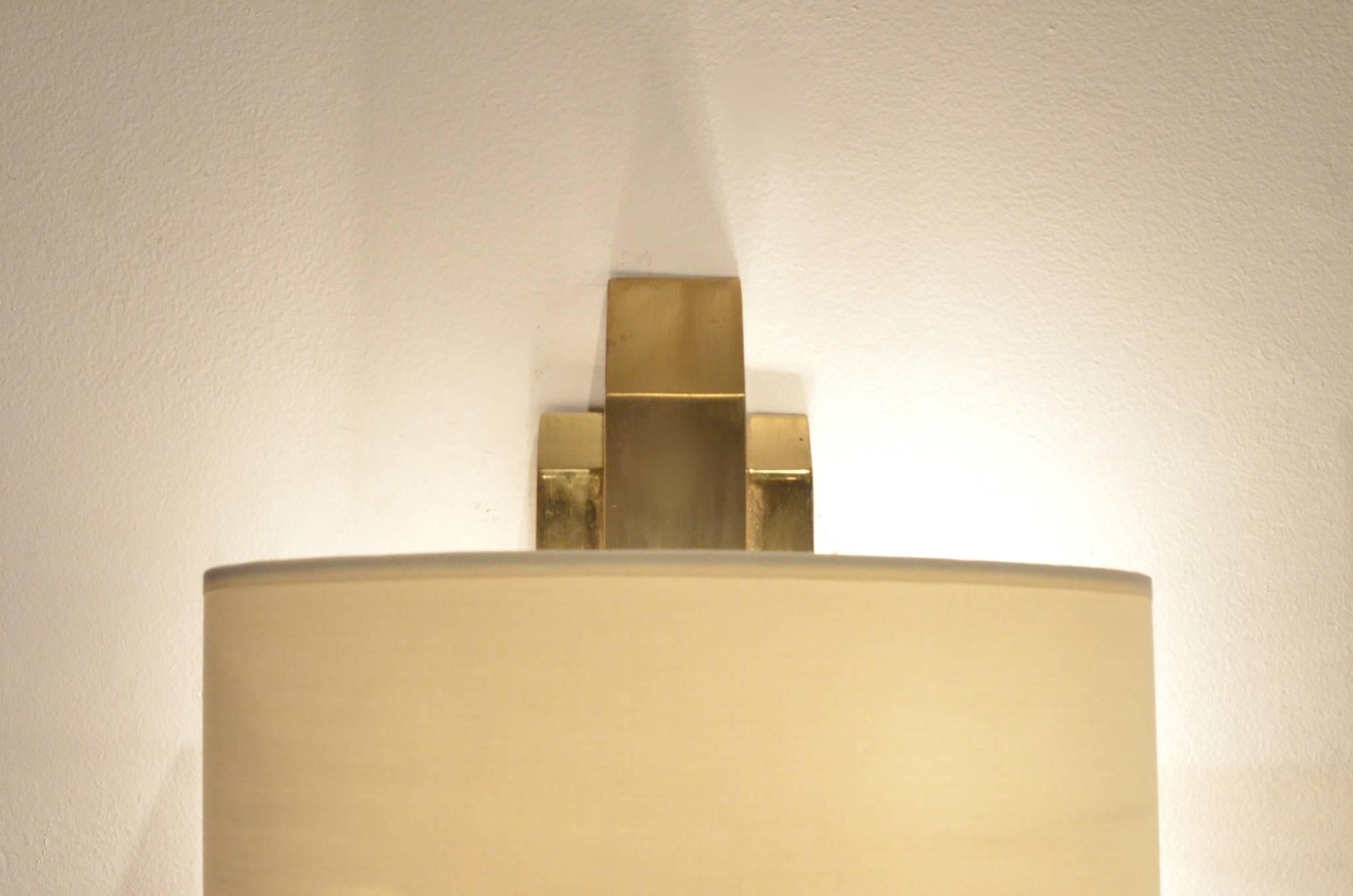 Elegant set of 2x German geometrical full brass structure wall sconces. Vernished and brushed brass elements matched with white textile shades.