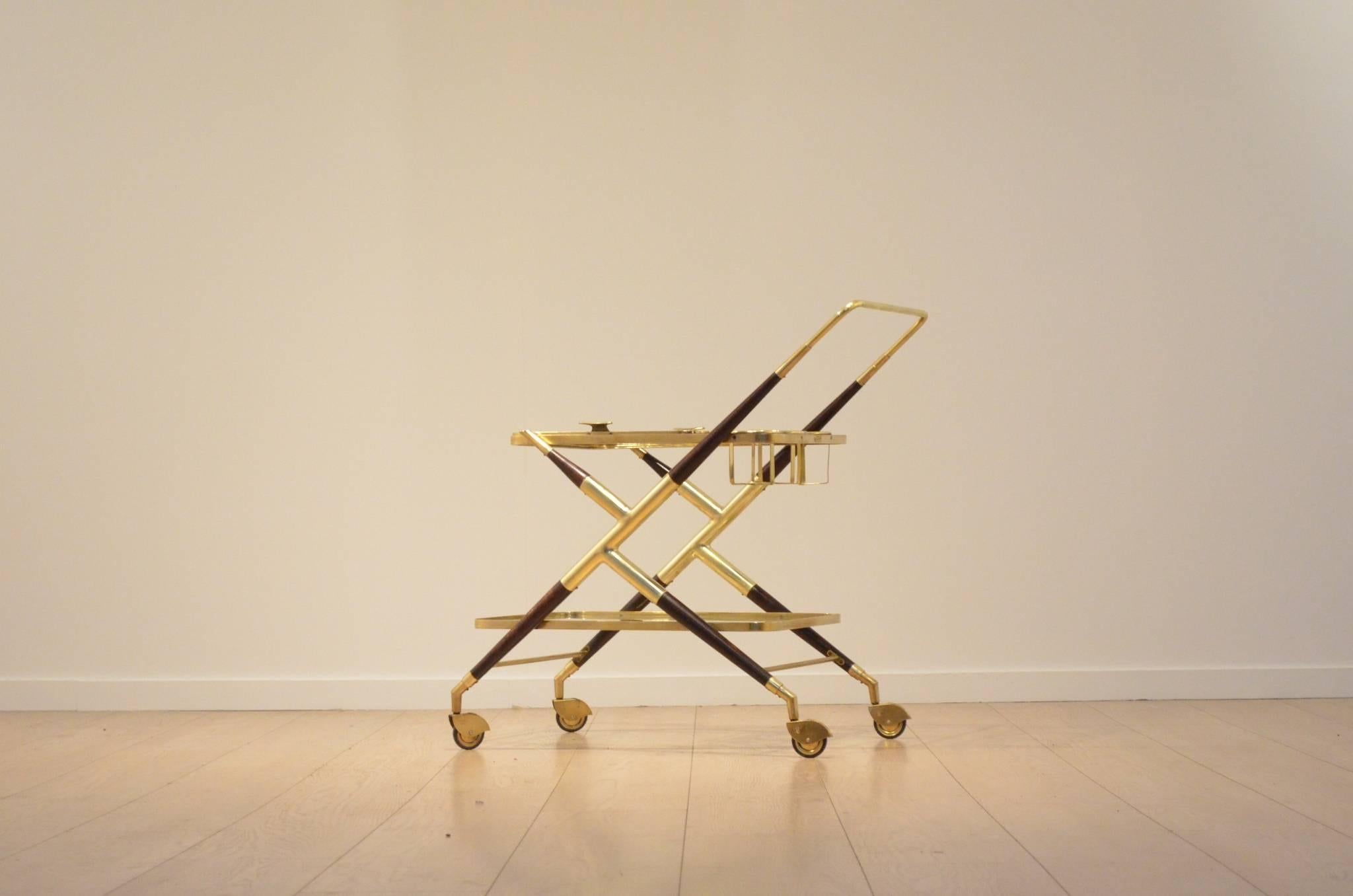 Italian 1950s Cesare Lacca serving trolley / bar with a zig zag shaped profile made in mahogany and brass, with three bottle holders placed near the handlebar of the trolley.

The first table surface made in glass and brass doubles up as a serving
